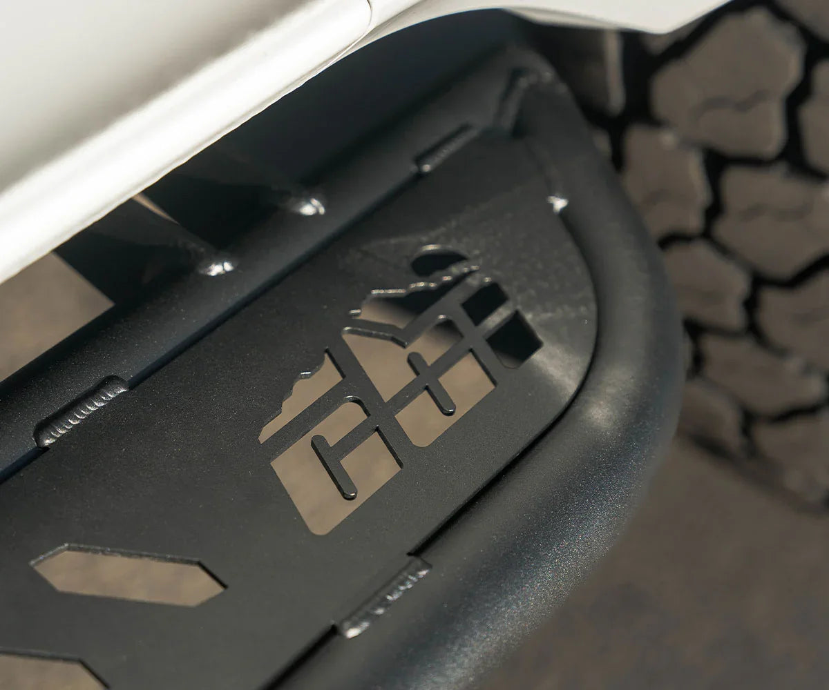 Close-up of black metal rock slider with mountain cutout on a Toyota 4Runner, off-road tire visible