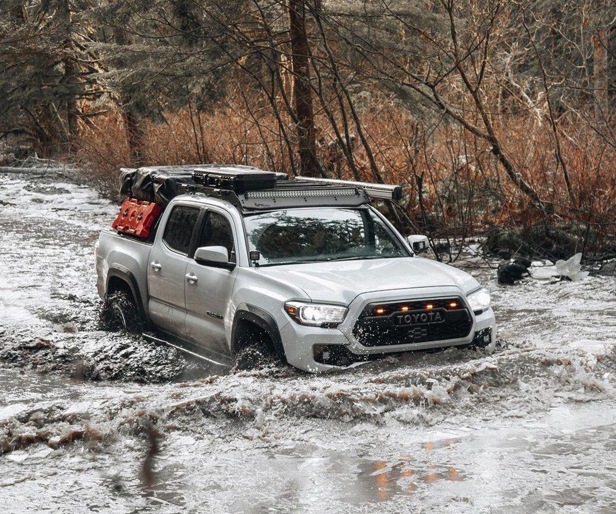 Toyota Tacoma overland truck crossing river with camping gear, off-road adventure scene