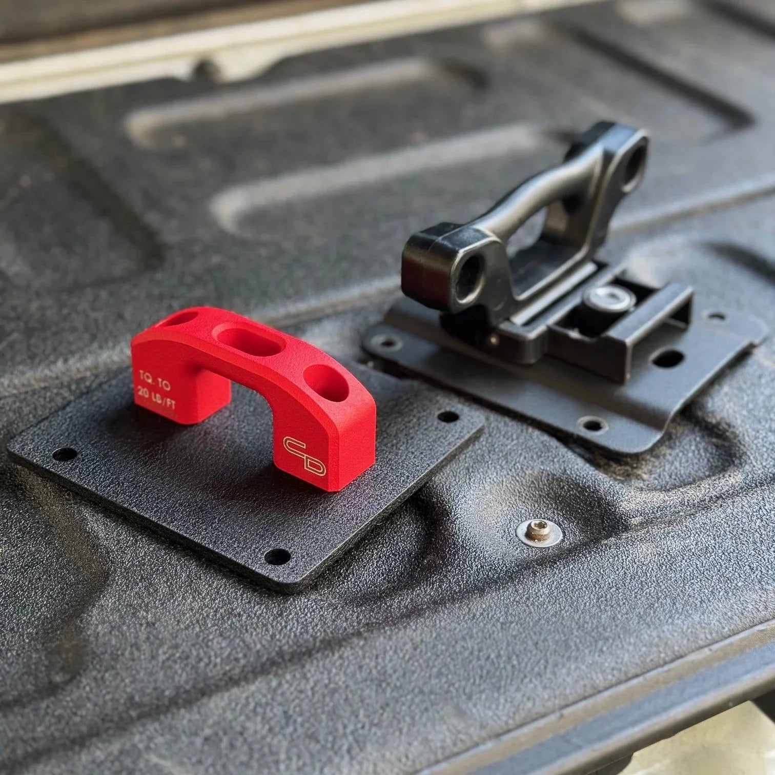 Red billet tie down anchor and black mounting bracket on truck bed for overlanding gear