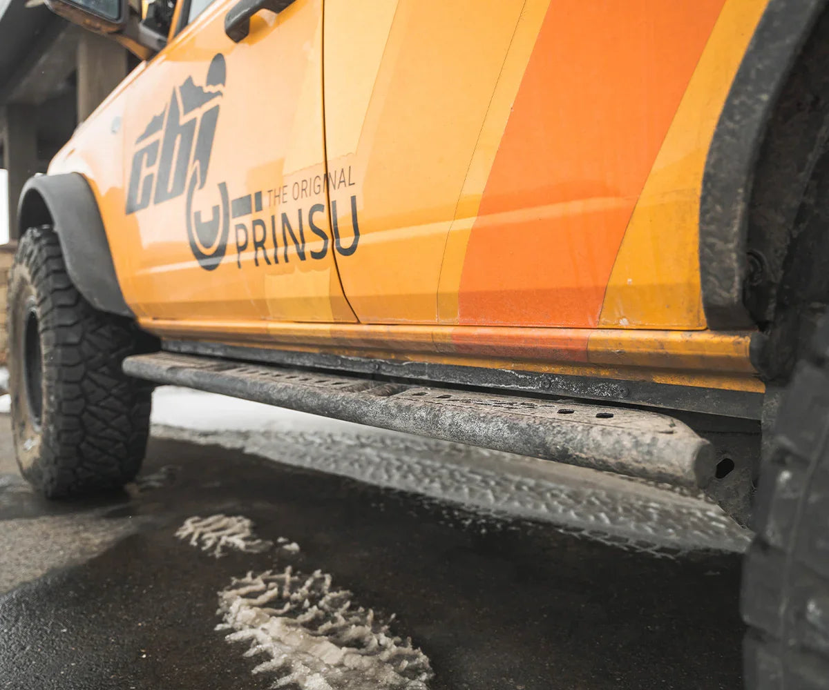Bolt-on rock sliders with weld plate mounted on orange Ford Bronco for off-road protection