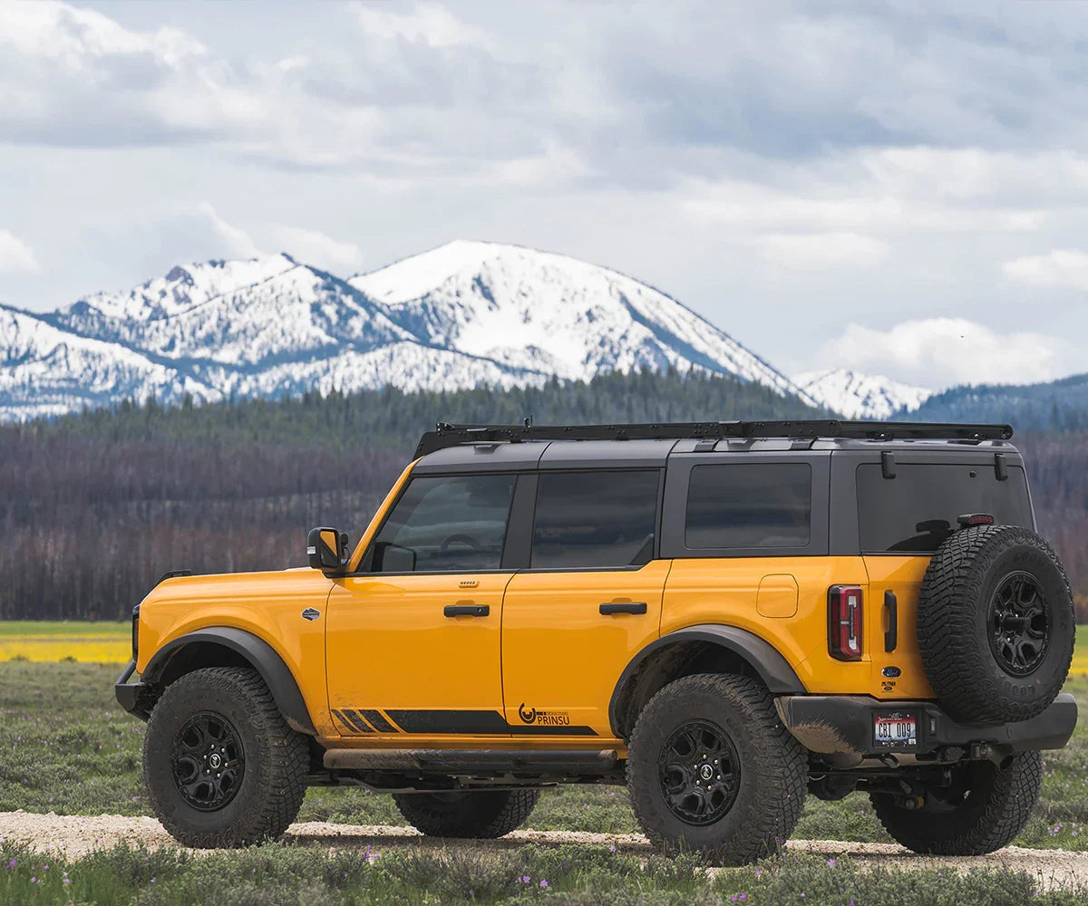 Yellow Ford Bronco overland build with roof rack and off-road tires parked outdoors, snowy mountains in background
