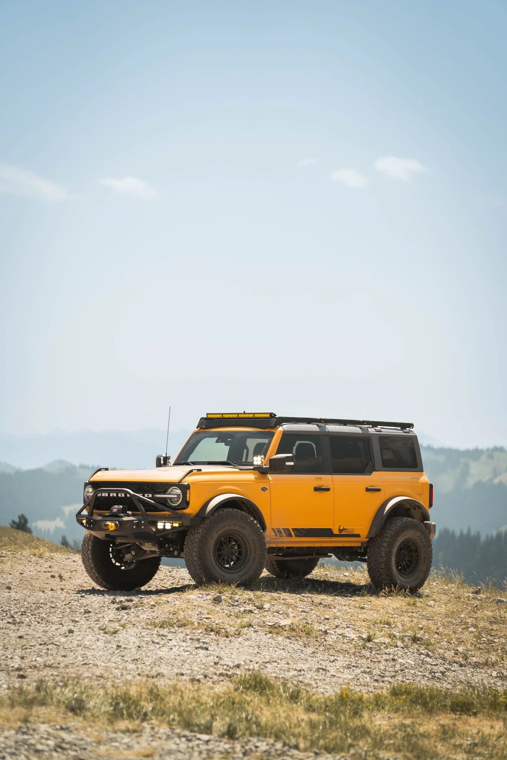 Yellow Ford Bronco SUV with off-road wheels and accessories on a mountain trail
