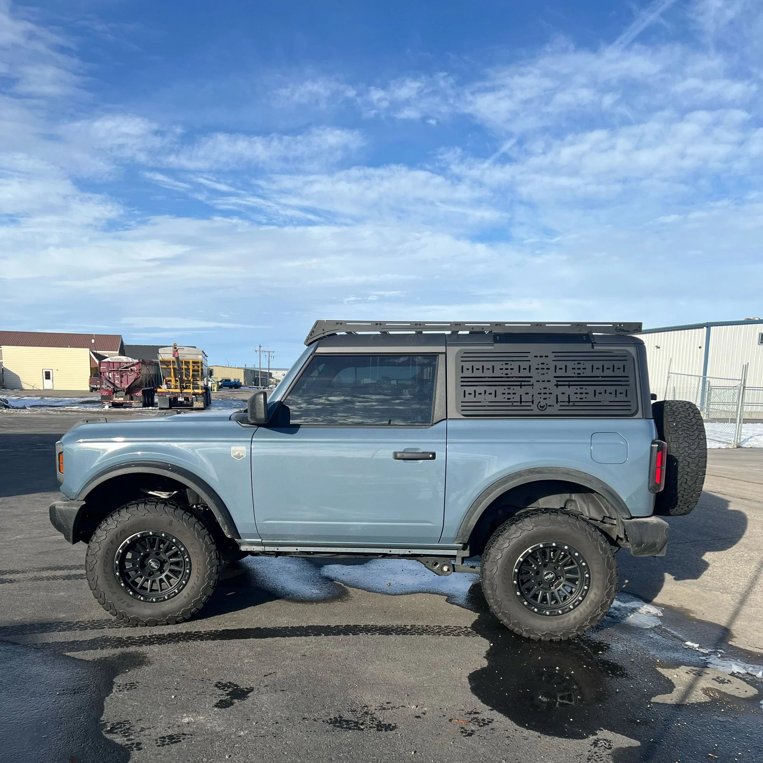 Ford Bronco with off-road tires, roof rack, and MOLLE panel, parked outdoors