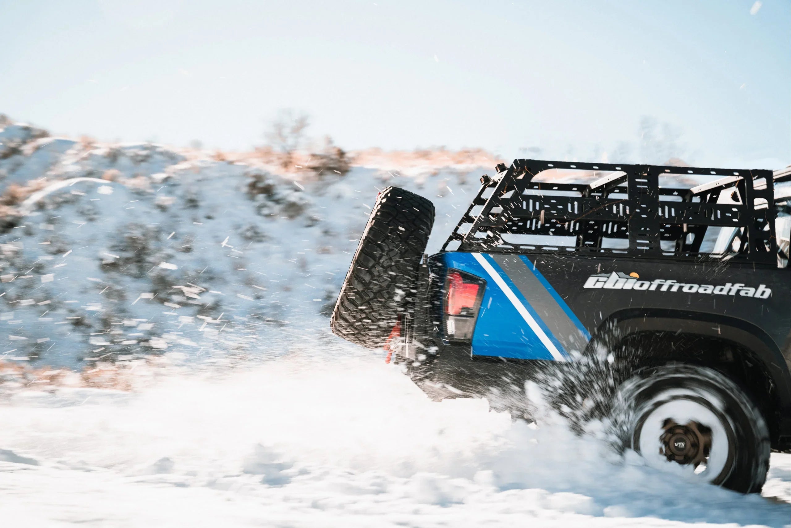 Off-road truck with spare tire and cargo rack driving through snowy terrain