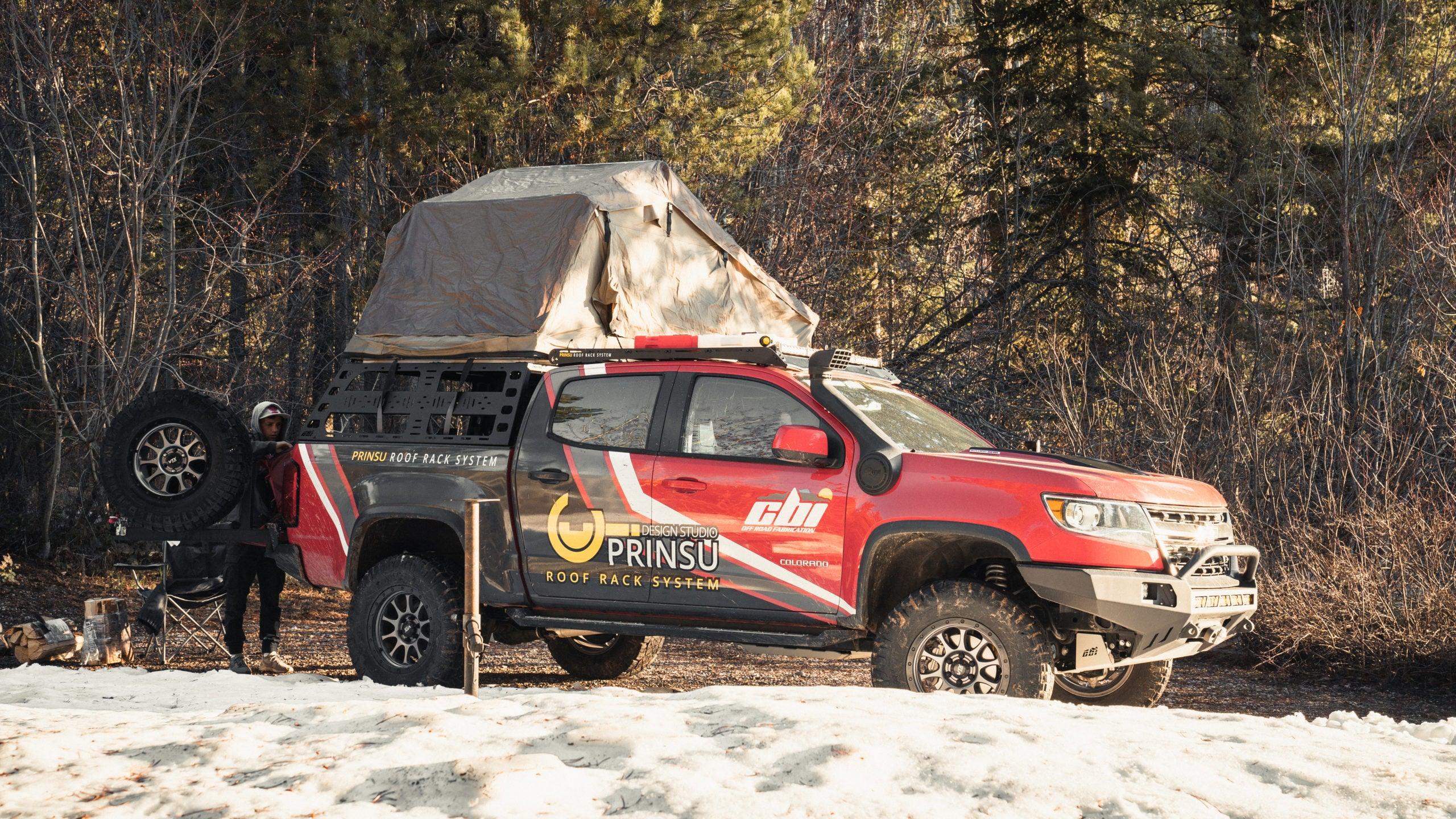 Chevy Colorado with sheet metal bed rack, rooftop tent, and overlanding gear parked in snowy forest.
