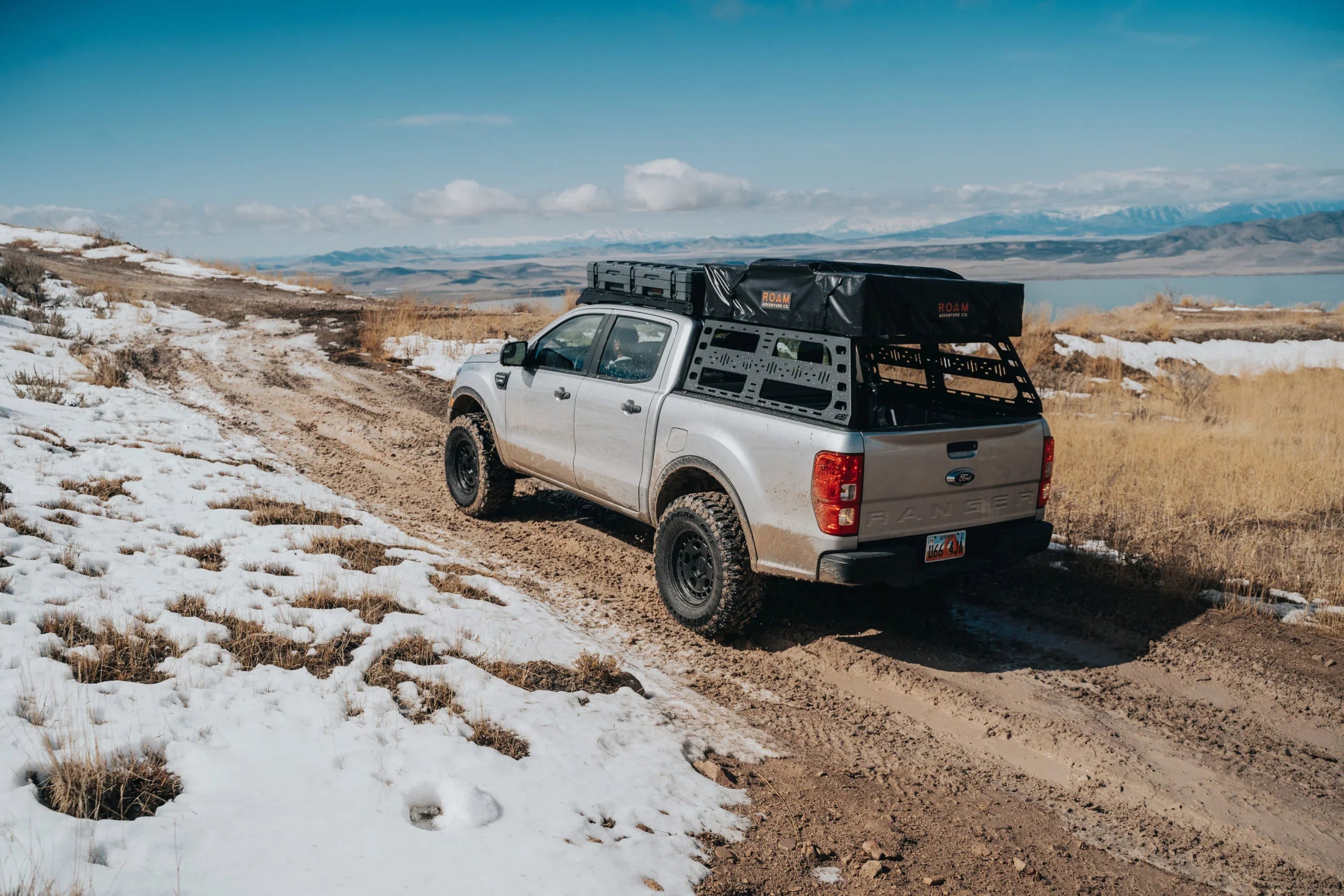 Ford Ranger with cab height bed rack, off-road gear, driving on a snowy dirt trail