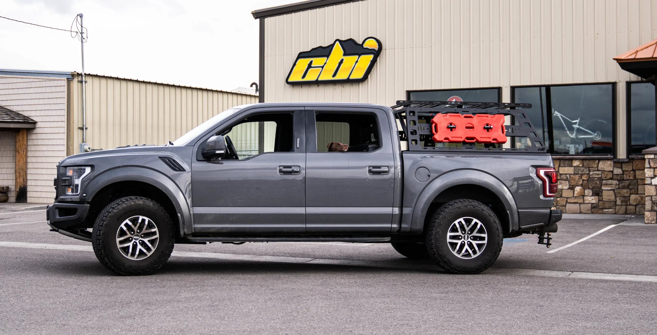 Ford Raptor with cab-height bed rack and mounted storage gear in parking lot