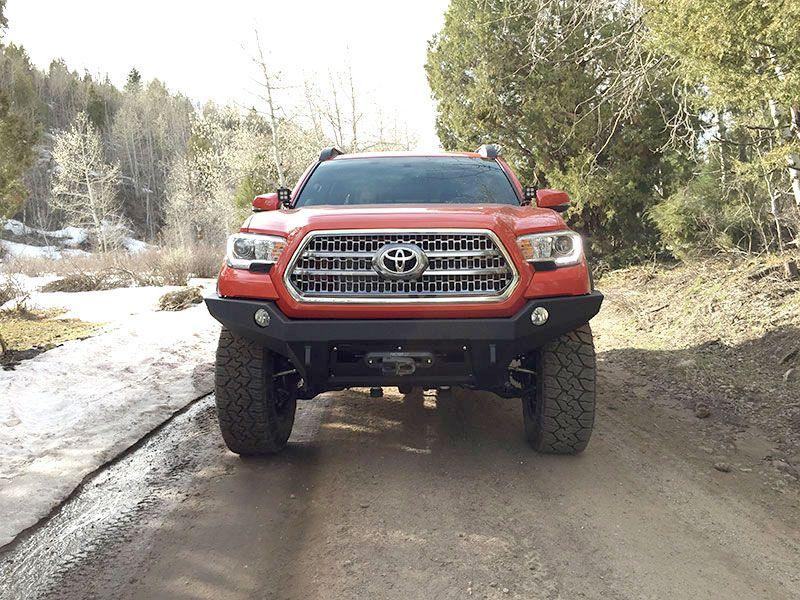 Red Toyota Tacoma with classic front bumper on off-road dirt trail, forest background