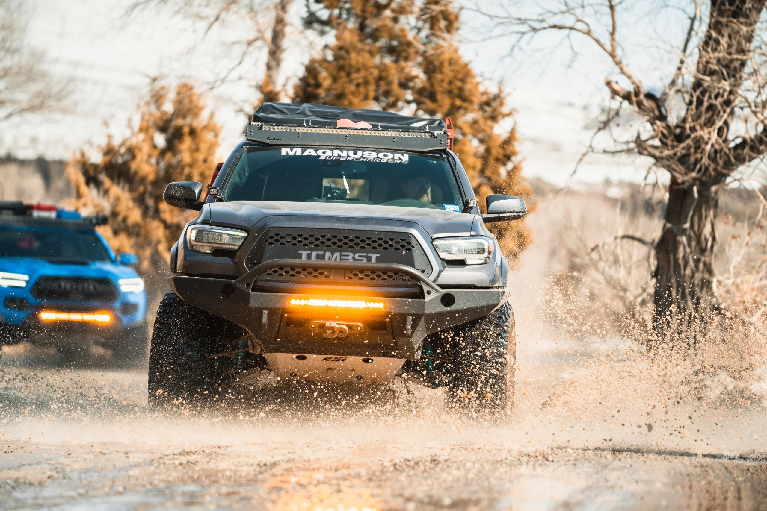 Toyota Tacoma with off-road bumper, roof rack, light bar driving through mud on a trail