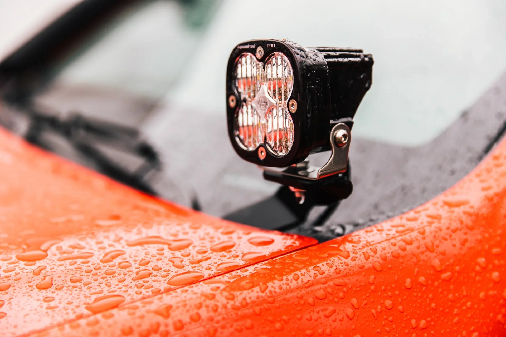 Close-up of LED off-road light mounted on wet orange vehicle hood, overlanding accessory
