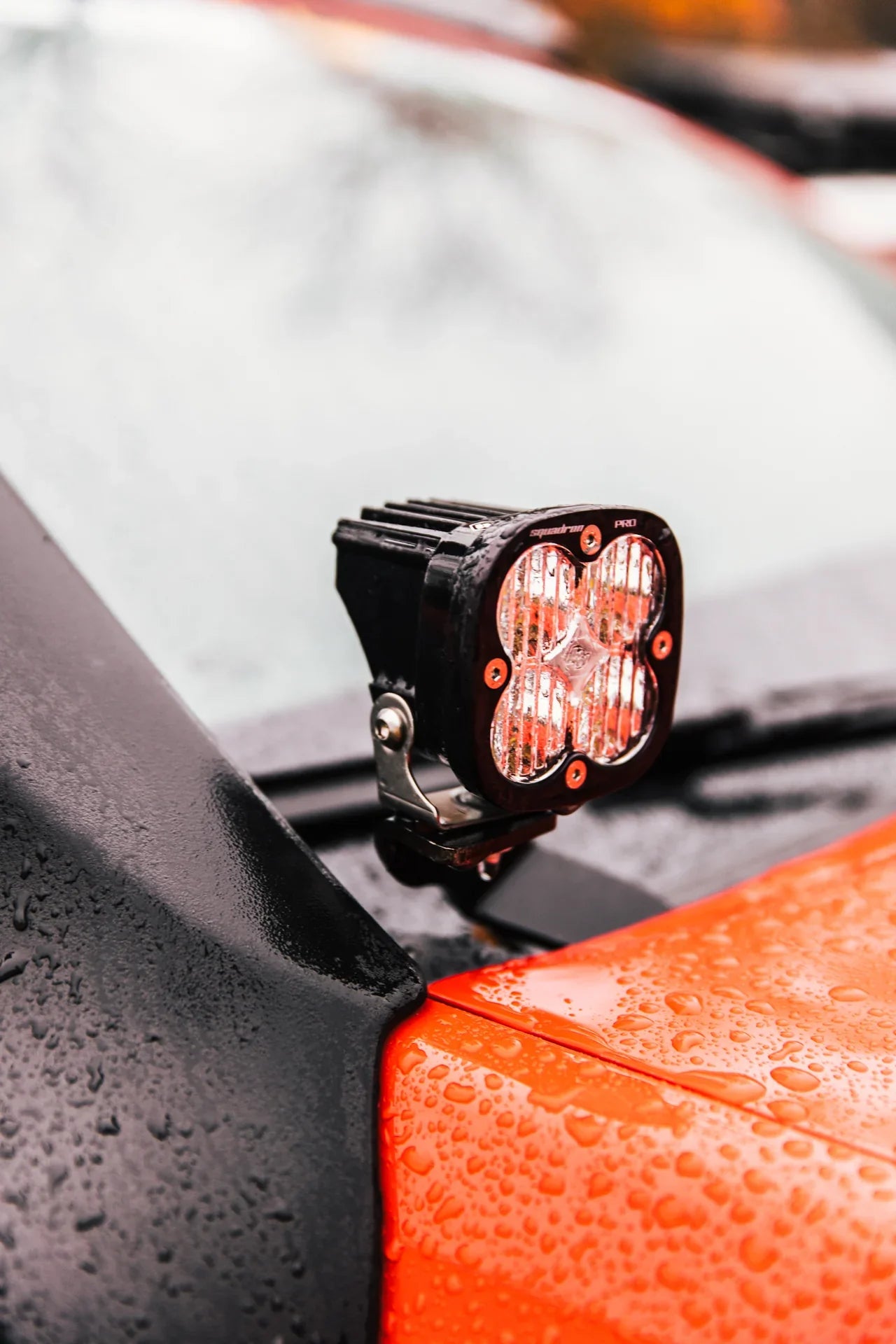 Close-up of off-road LED pod light mounted on orange overland vehicle hood in rain