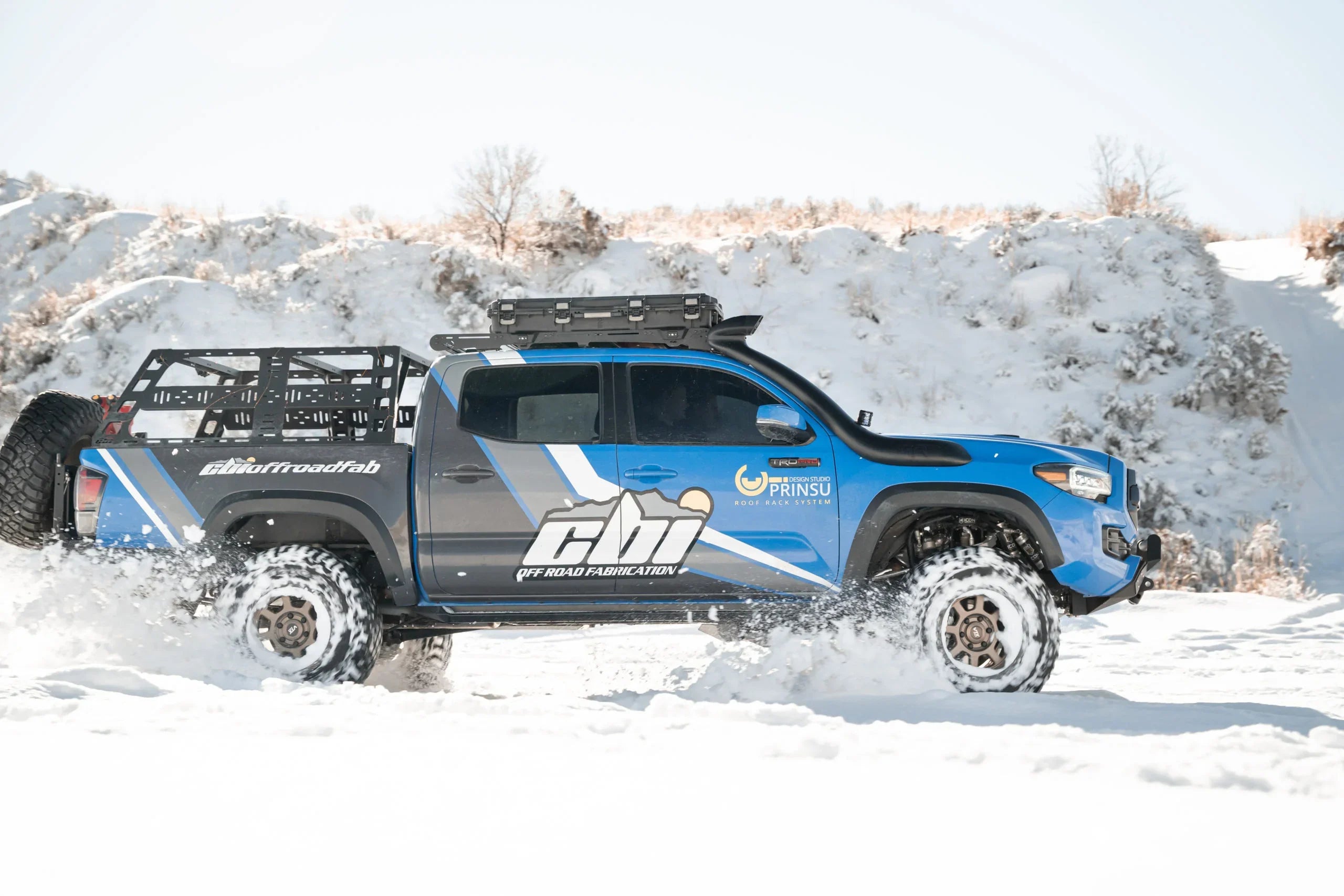 Toyota Tacoma with off-road accessories driving through snow, roof rack, bed rack, rugged tires