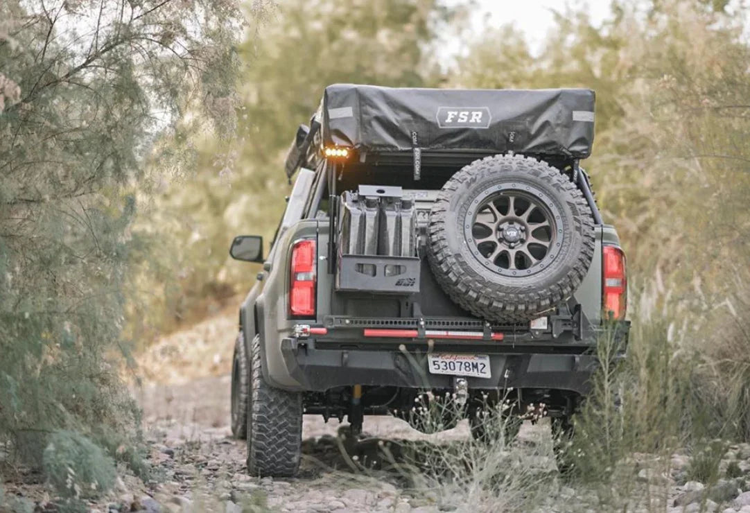 Overland vehicle with rooftop tent, spare tire, and gear driving off-road in nature