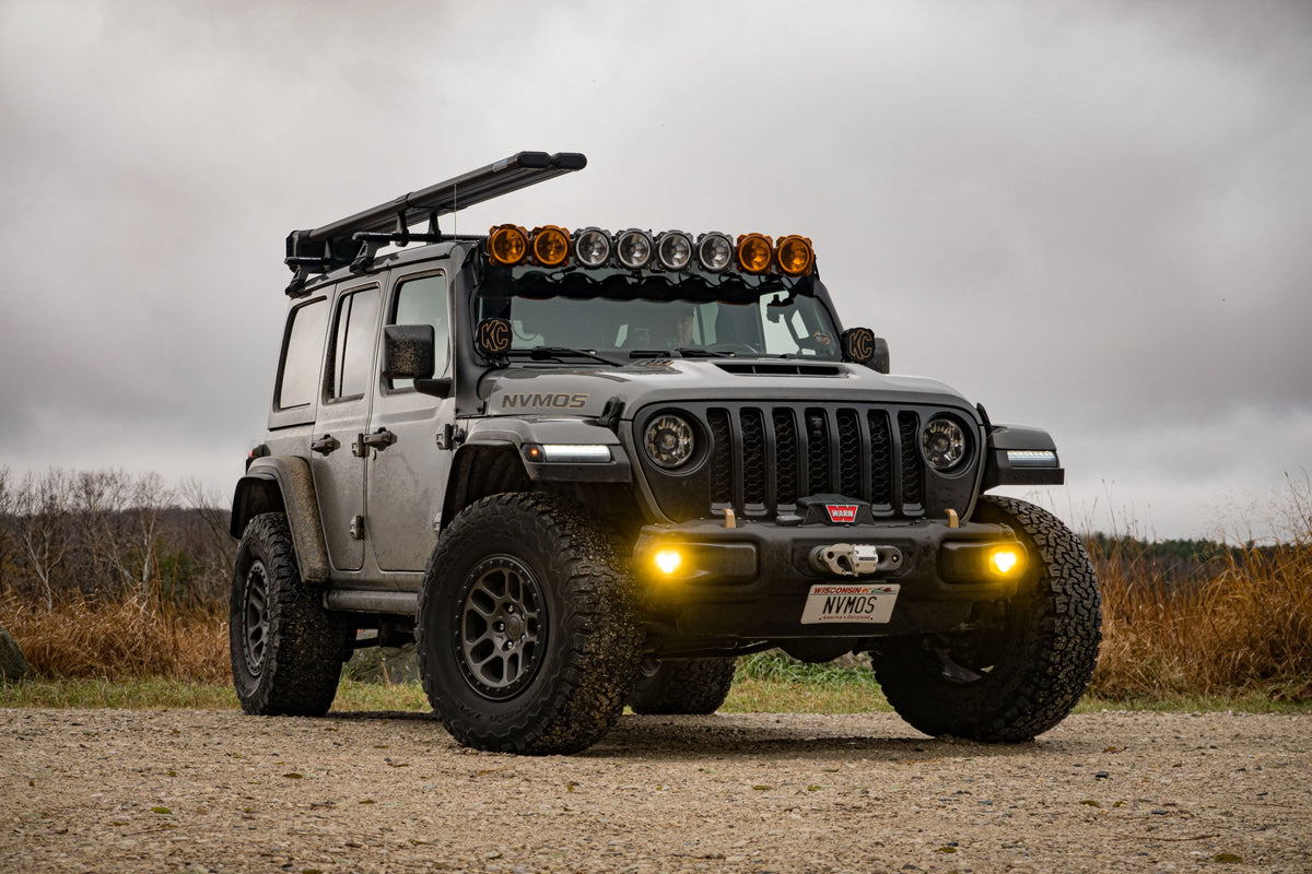 Jeep Wrangler with roof rack, off-road lights, mud tires, and overlanding gear outdoors