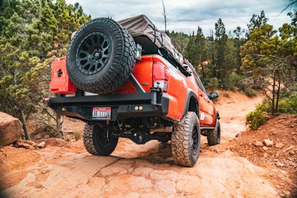 Chevy Colorado with off-road swing arm bumper, spare tire, and gear on rocky trail