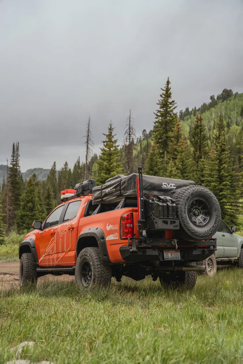 Orange Chevy Colorado ZR2 with rear bumper swing arms, spare tire, overlanding gear in forest