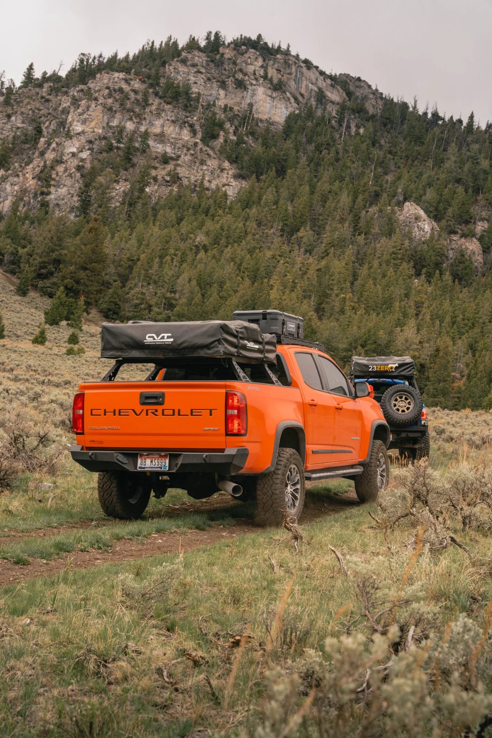 Orange Chevrolet Colorado ZR2 with camping gear and side steps on off-road trail in mountains
