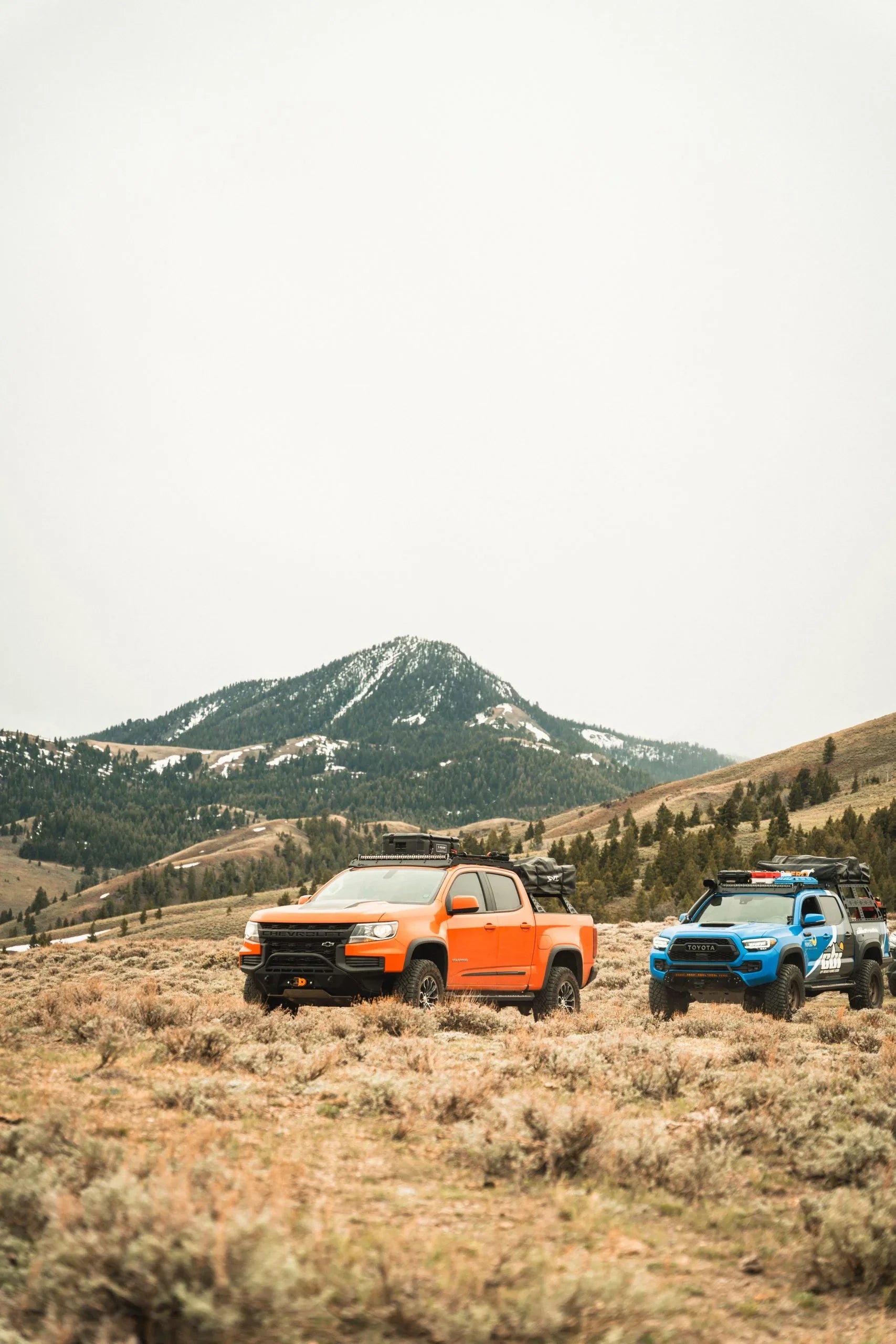 Overland trucks with camping gear in a mountain landscape, Chevrolet Colorado and Toyota Tacoma