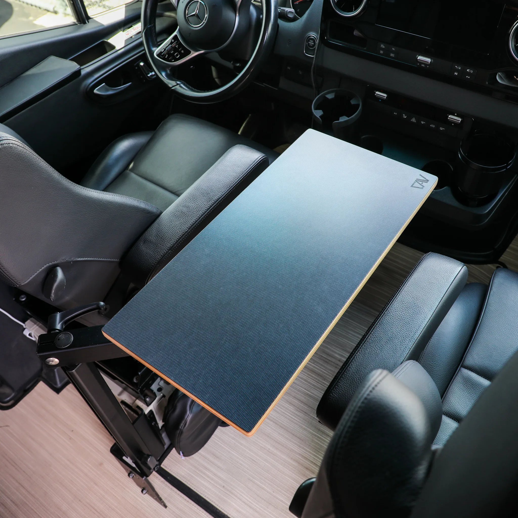 Van front cabin with foldable swivel table between black leather seats, Mercedes dashboard