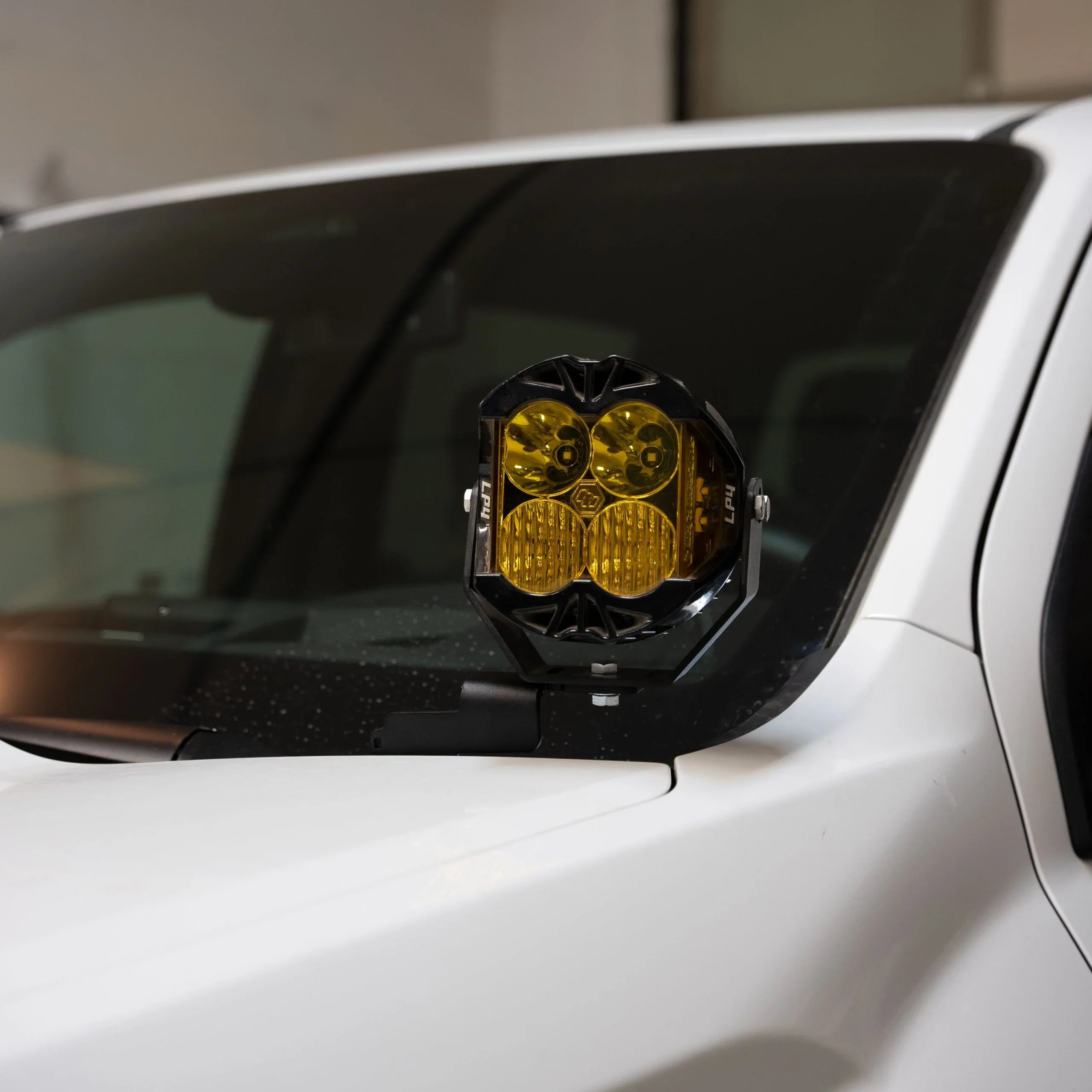 Yellow LED pod light mounted on white off-road vehicle's hood near windshield
