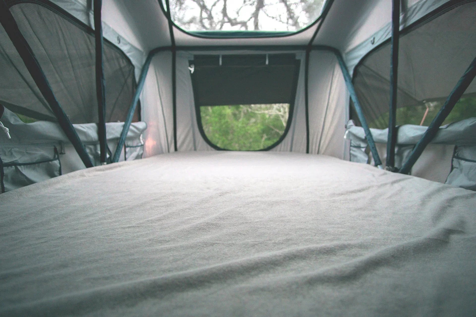 Spacious rooftop tent interior with mesh windows and green forest view, ideal for overlanding camping