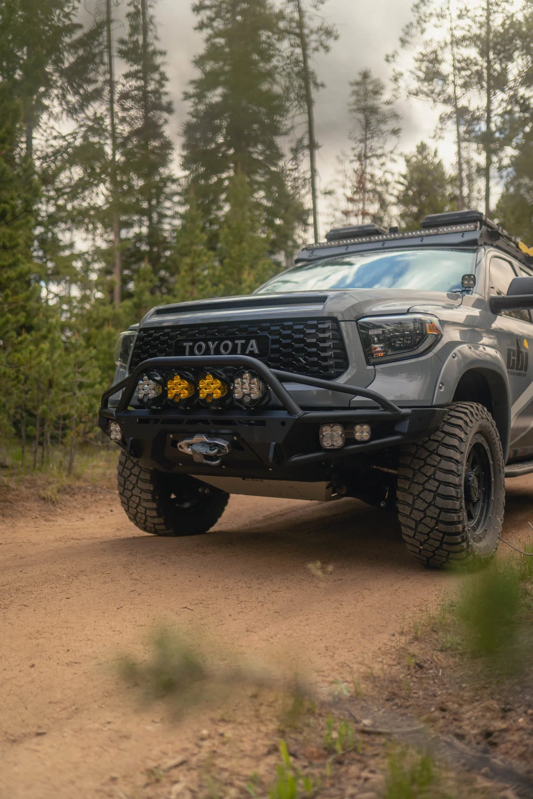 Toyota Tundra with off-road gear and rugged tires driving on a forest trail
