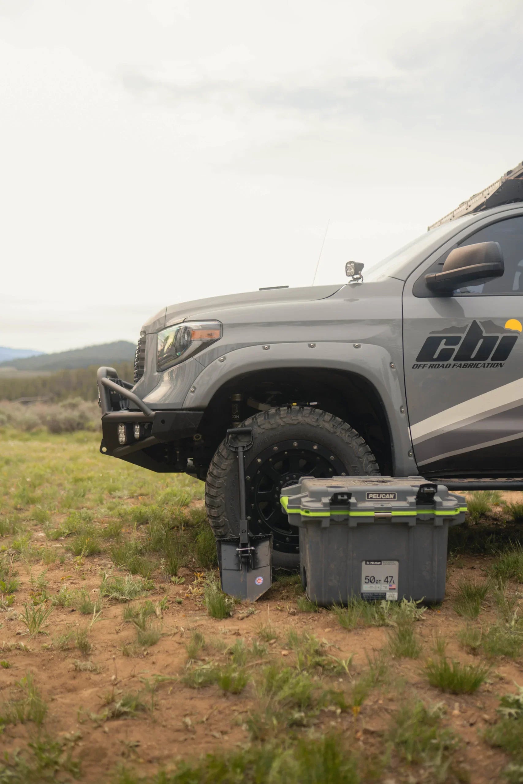 Off-road Tacoma truck with camping storage box and recovery shovel on grassy terrain