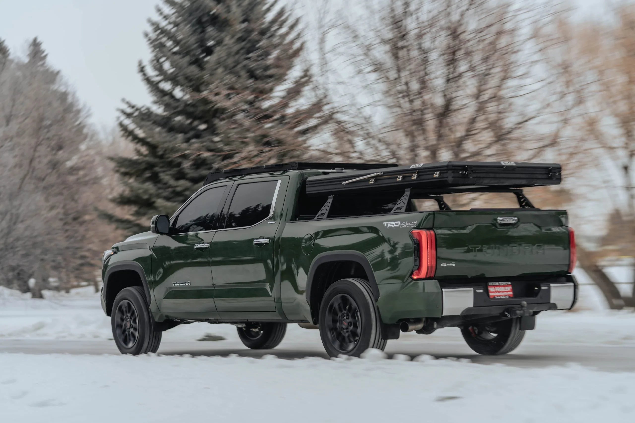Green Toyota Tundra with roof rack and overlanding gear driving in snowy outdoor setting