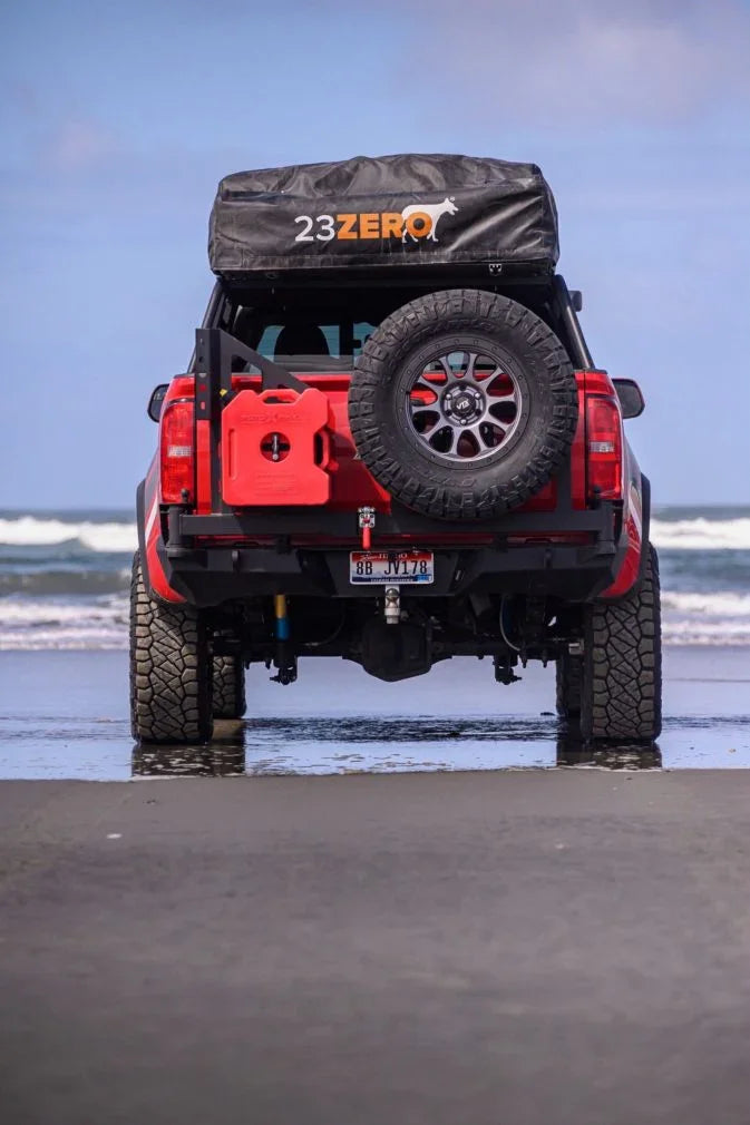 Overland truck with rooftop tent, spare tire, and fuel can on beach, ocean in background