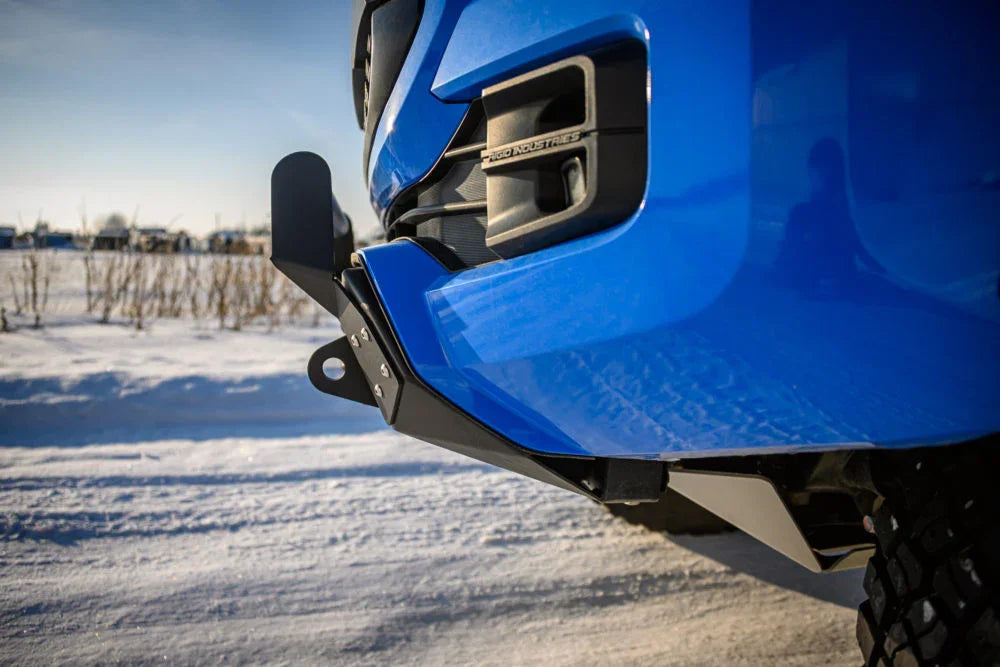 Blue off-road vehicle with aftermarket front bumper and recovery point in snowy landscape