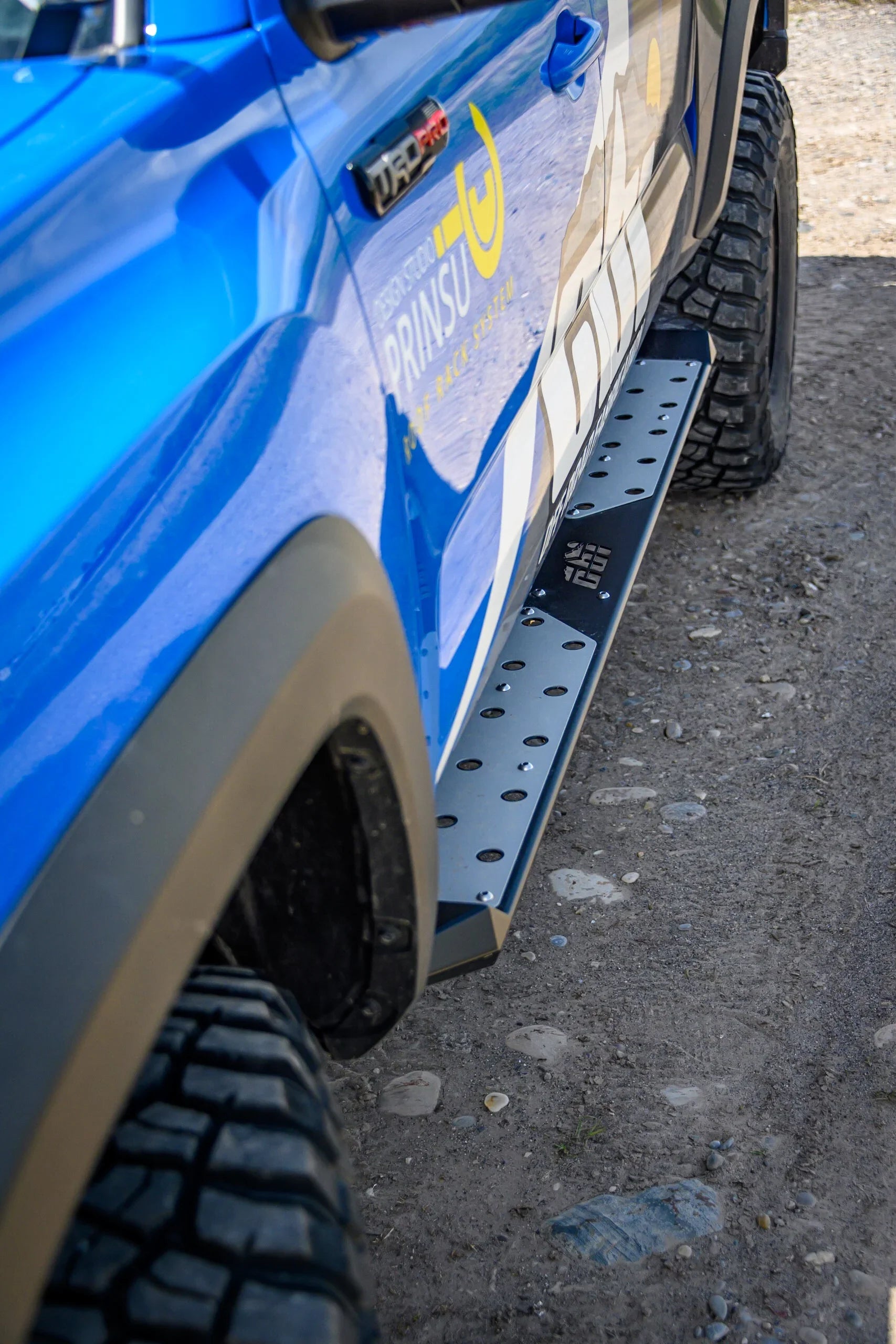 Blue off-road truck with rock slider step and rugged all-terrain tires on dirt road