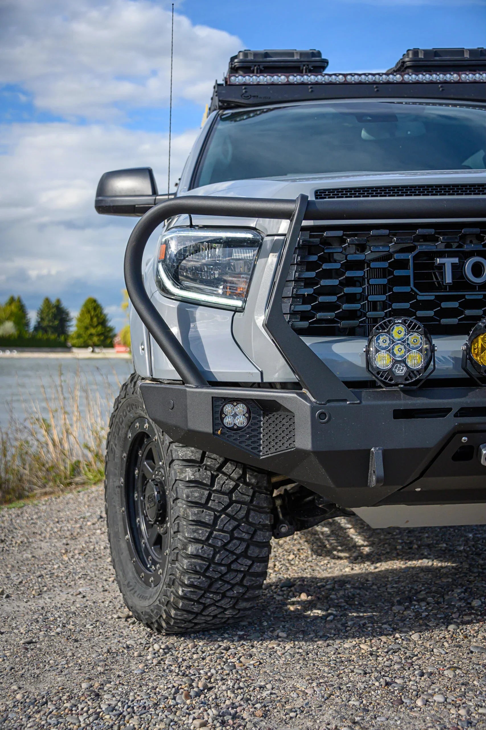 Toyota Tacoma with off-road bumper, LED lights, and roof rack on gravel by water
