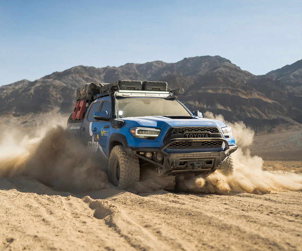 Blue Toyota Tacoma with Dakar hybrid front bumper driving off-road in desert mountains
