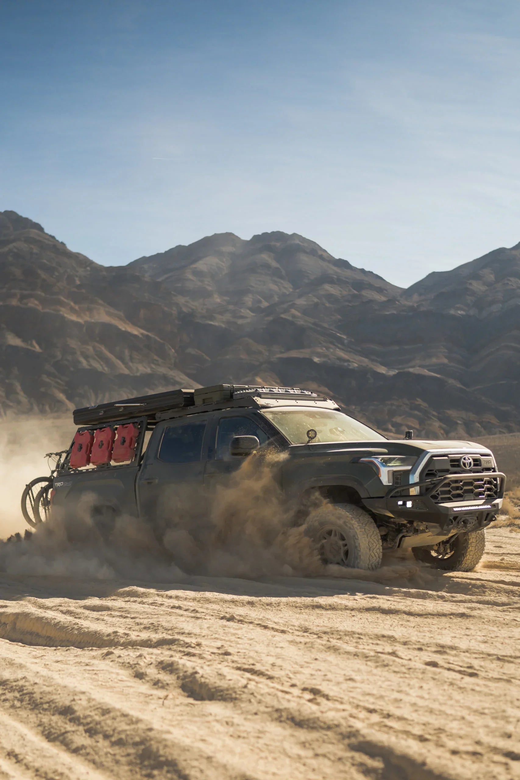 Toyota Tacoma overland truck with camping gear driving off-road in desert mountains