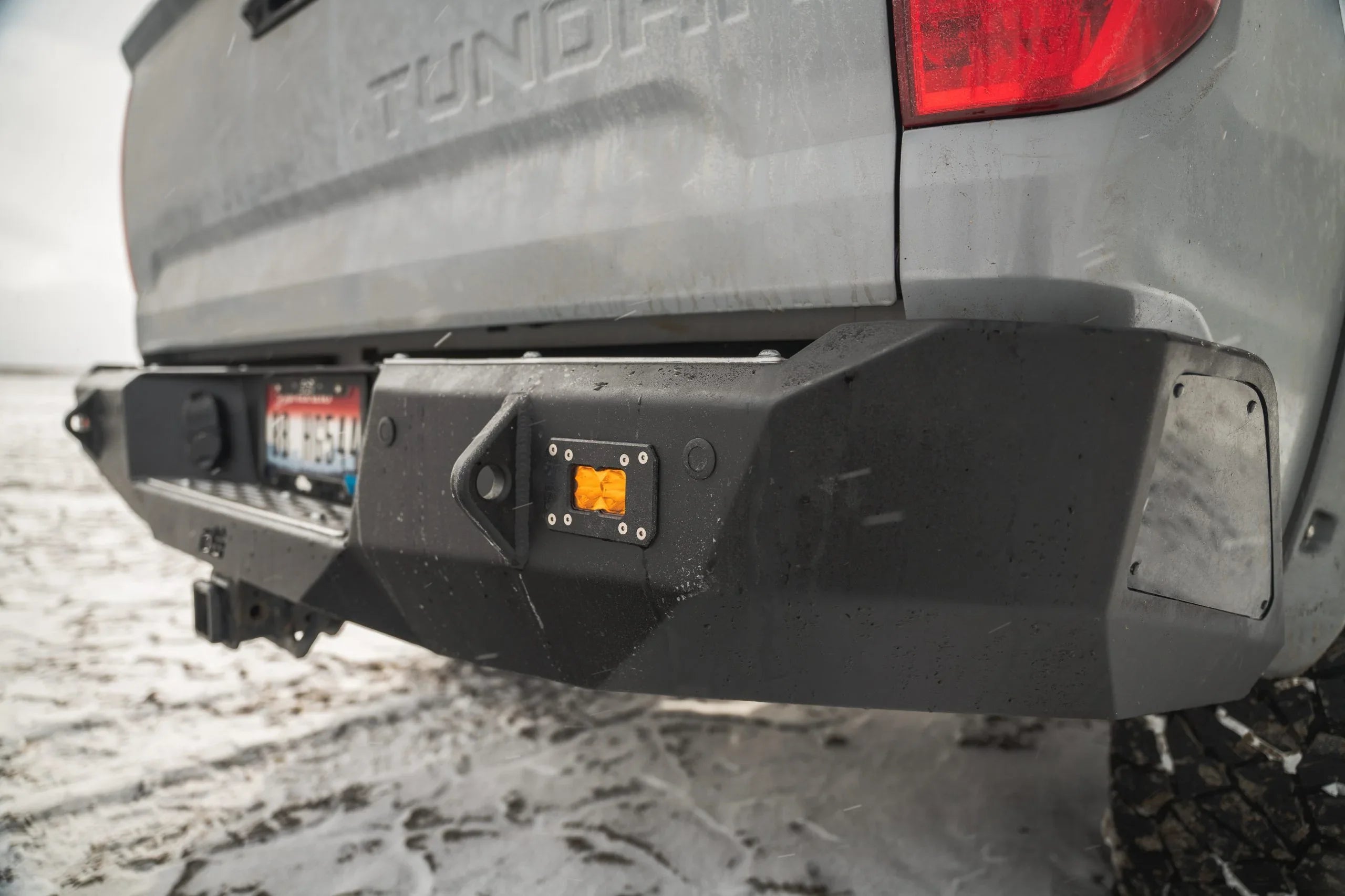 Toyota Tundra rear steel off-road bumper with tow hitch and amber light in snowy setting