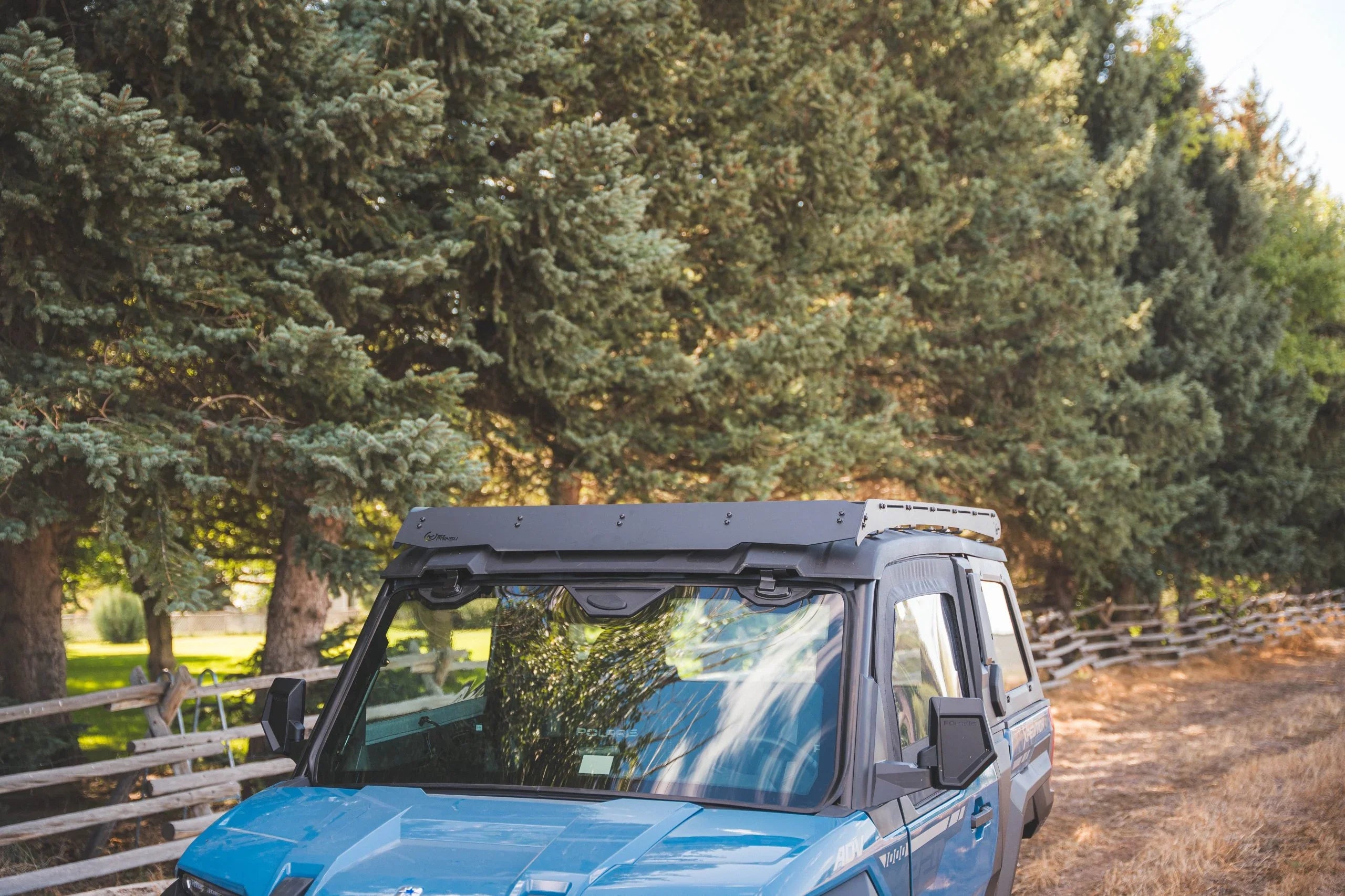 Blue off-road adventure vehicle with modular roof rack parked outdoors by pine trees