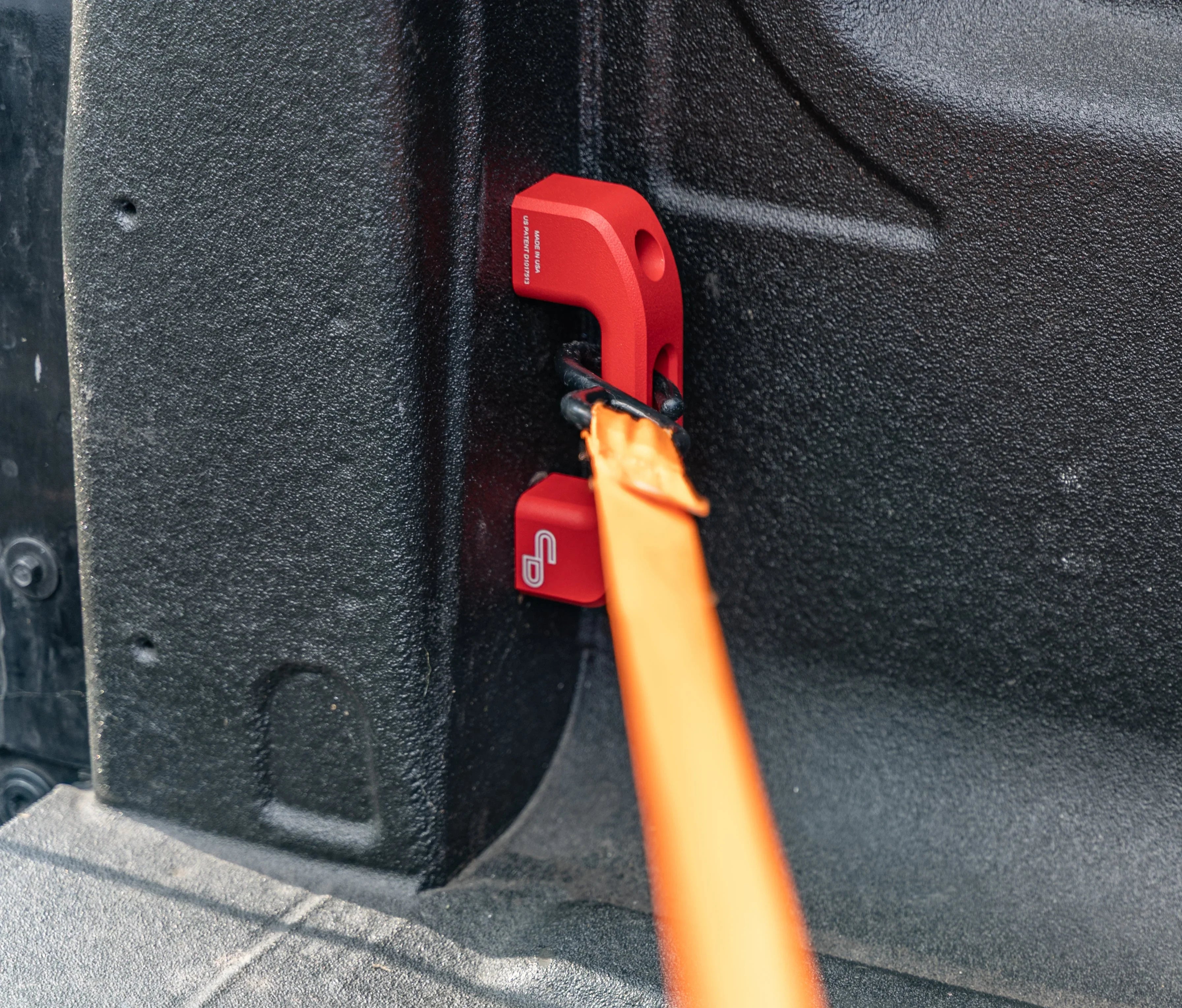 Red bed rail tie down anchor with orange strap in a truck bed, overlanding accessory