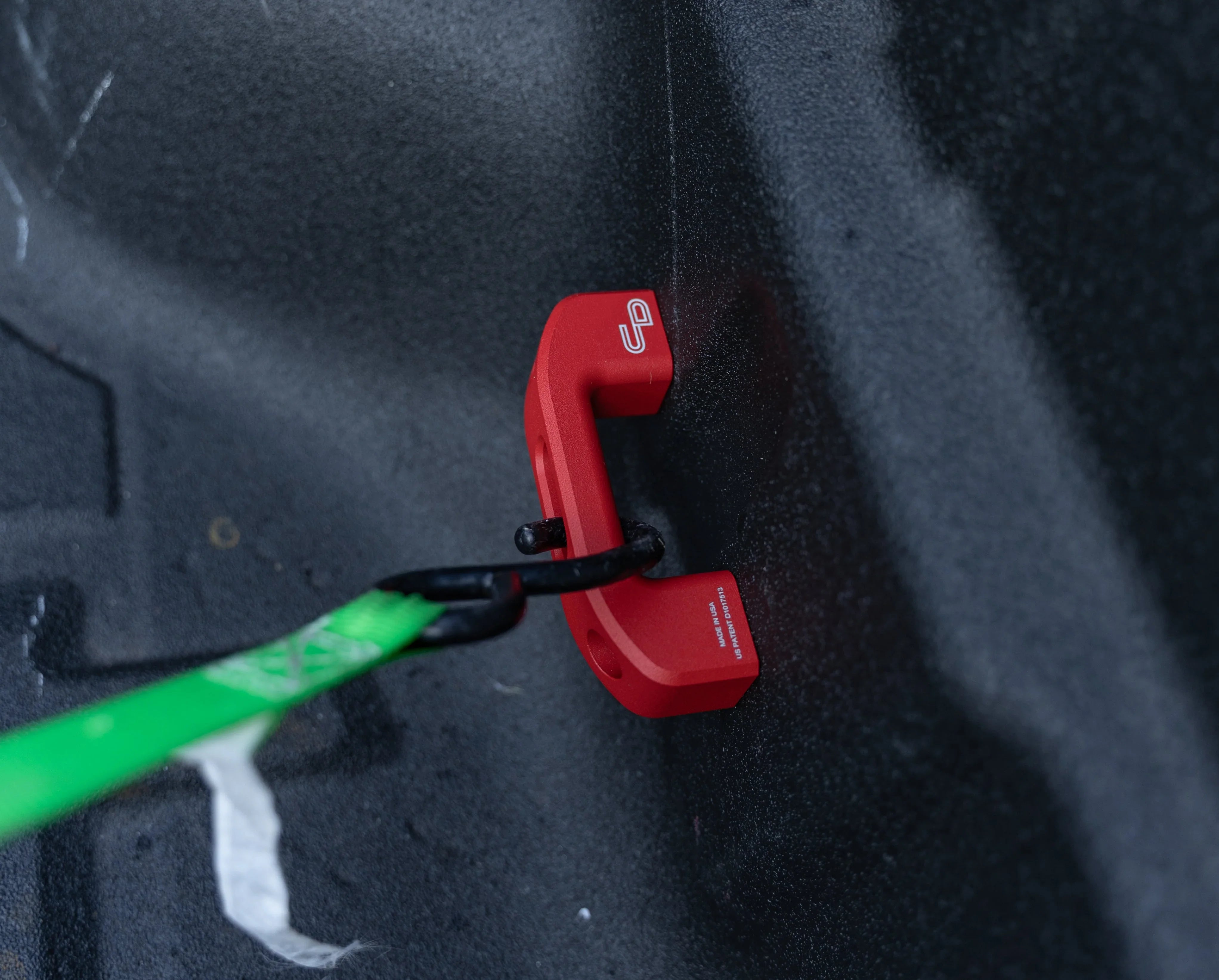 Red aluminum tie down anchor installed in truck bed with strap attached, vehicle accessory