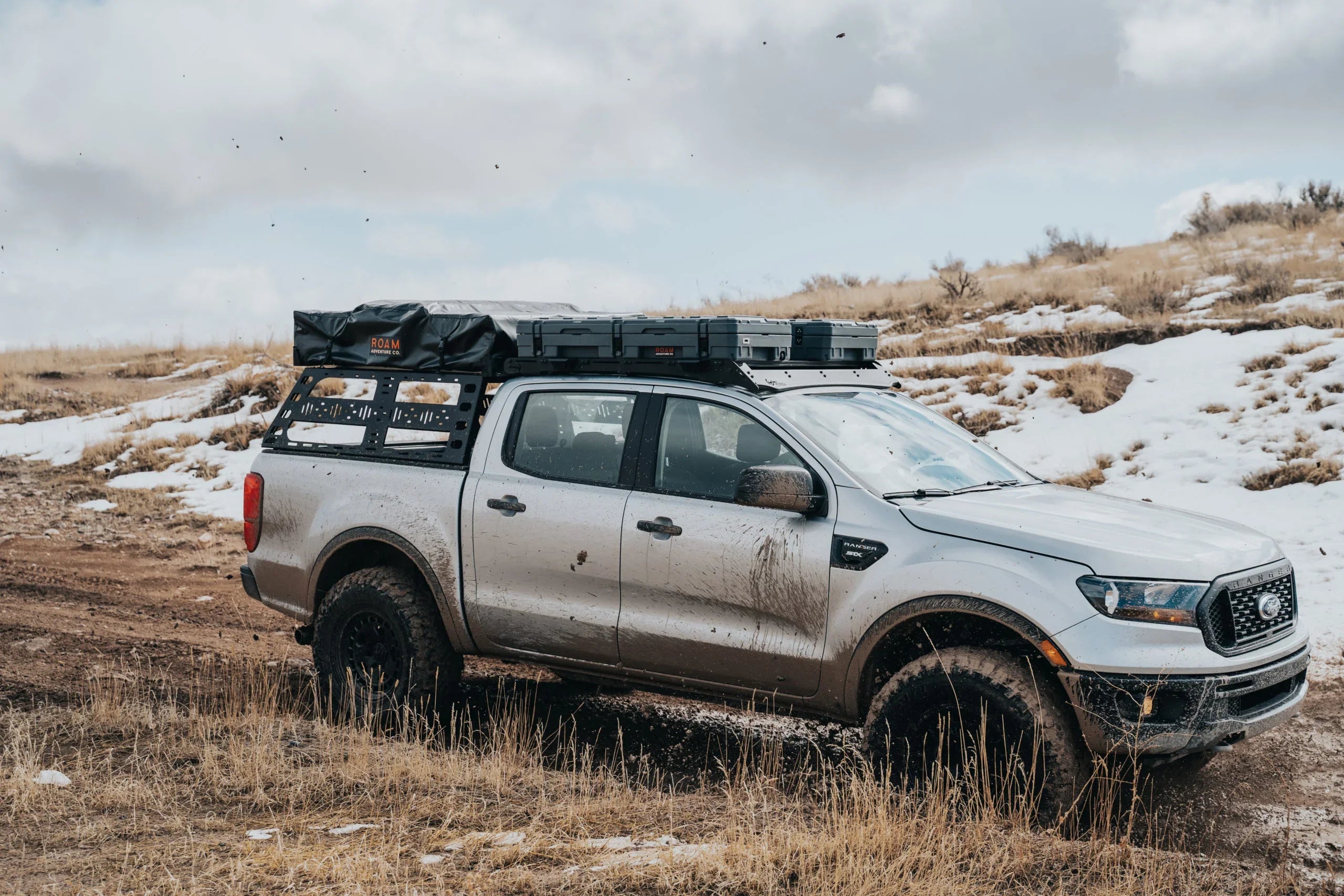 Ford Ranger with cab height bed rack, off-road gear and rooftop storage, driving on muddy trail