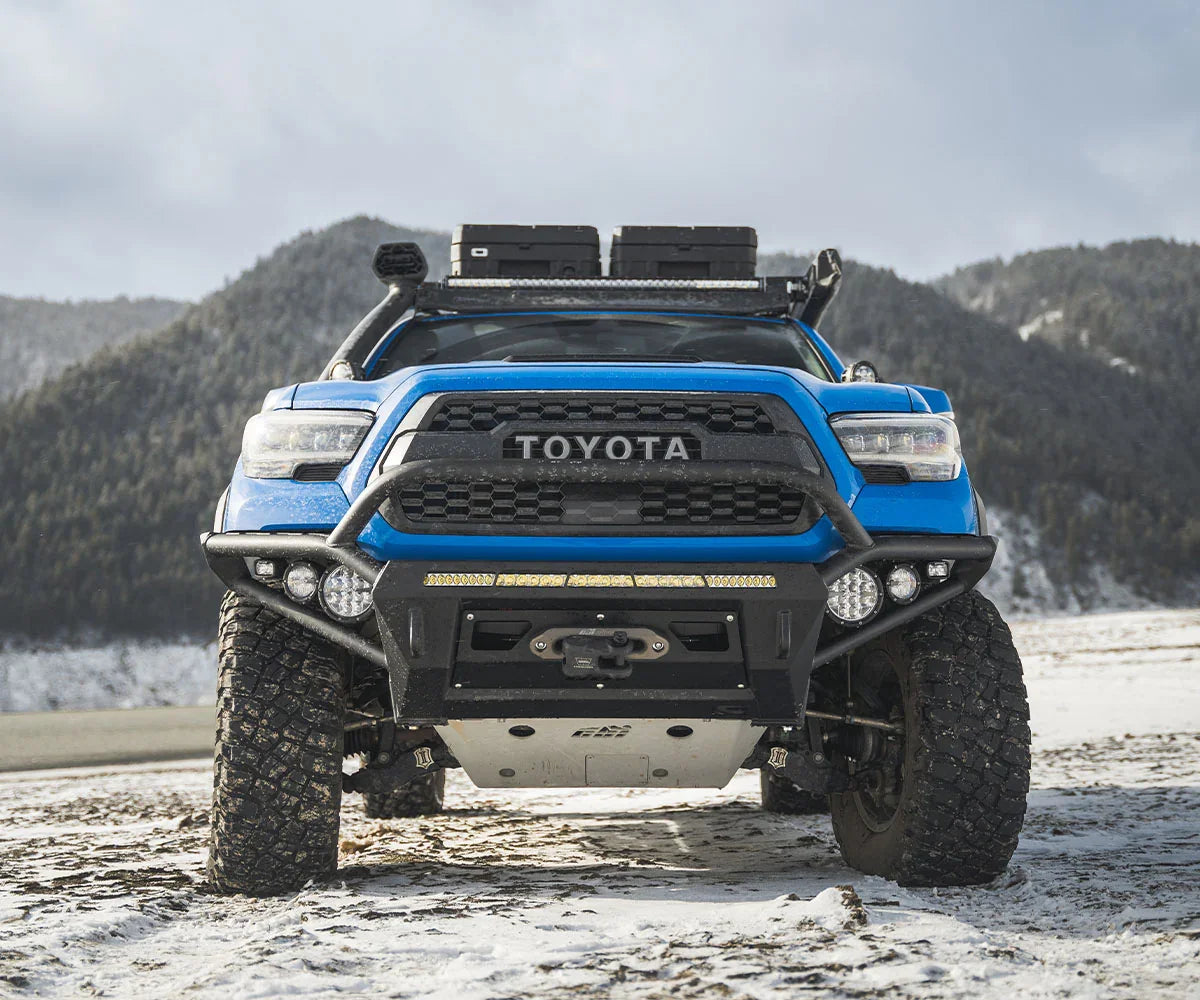 Toyota Tacoma with off-road front bumper and LED lights on snowy mountain terrain