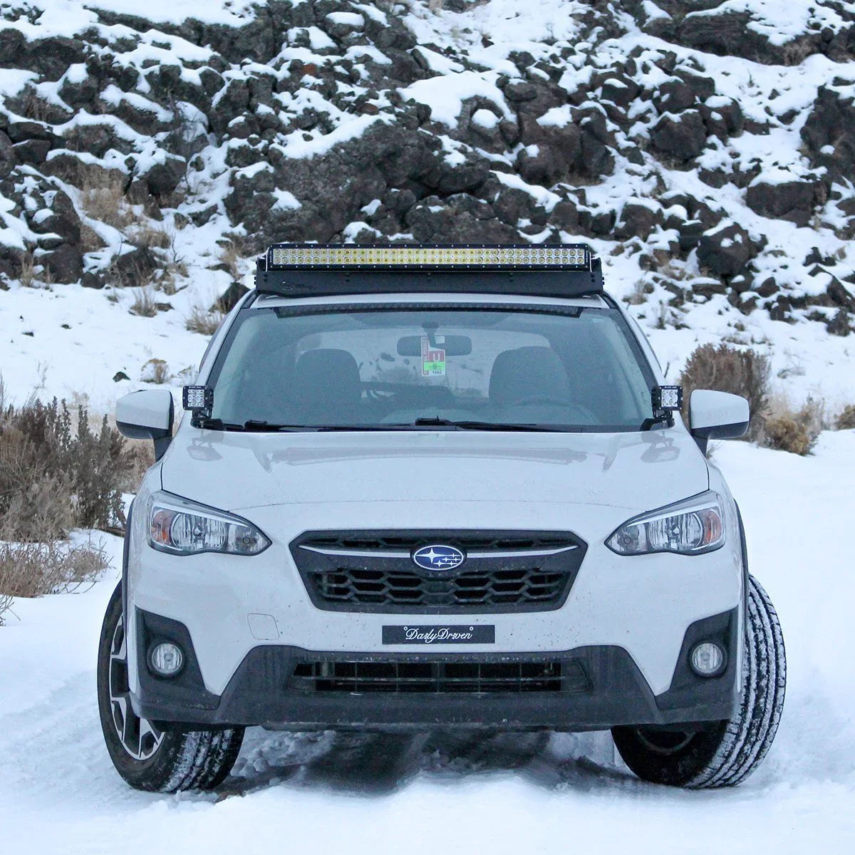 White Subaru SUV with roof-mounted LED light bar on snowy off-road trail