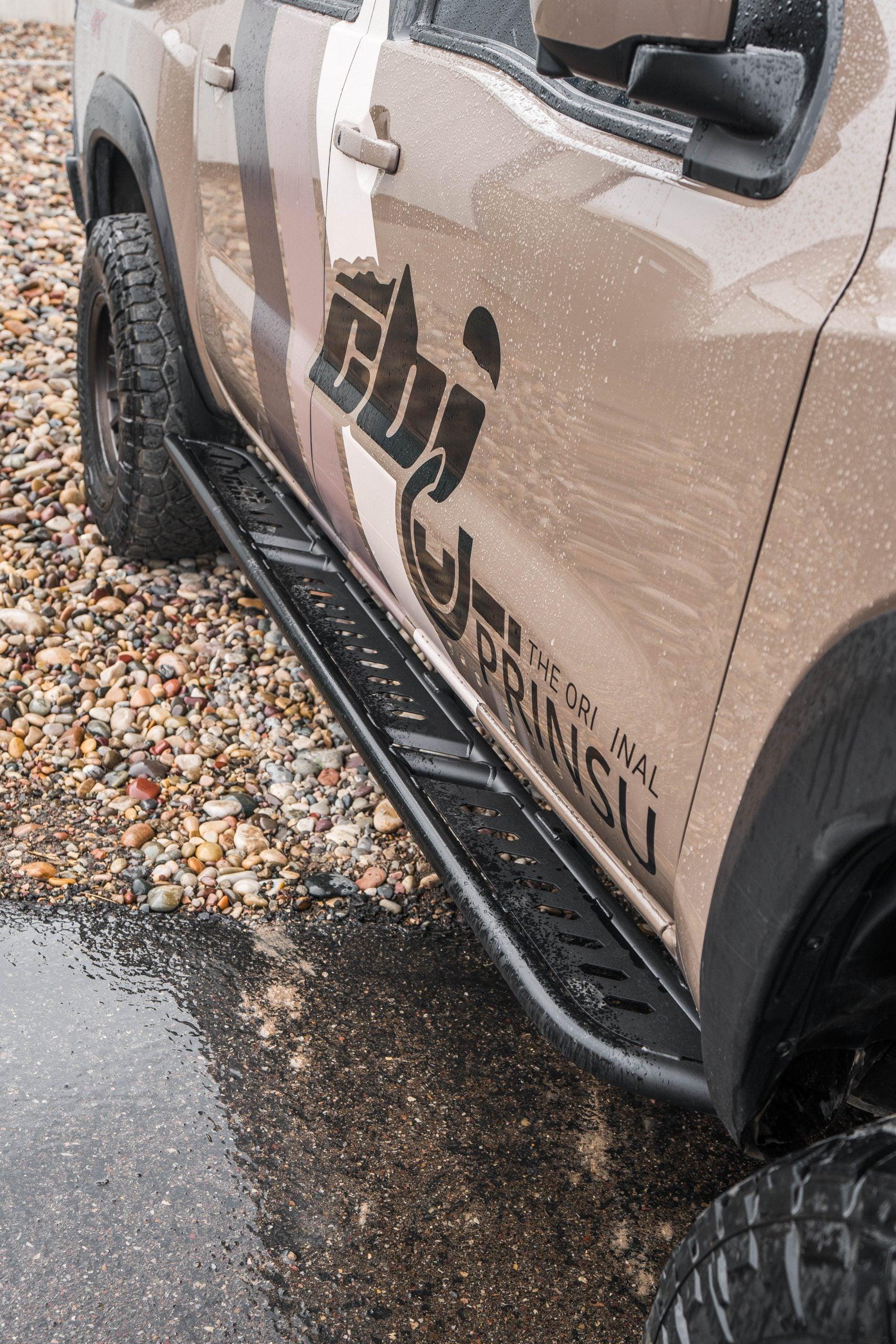 Heavy-duty rock sliders installed on an off-road vehicle parked on wet gravel.