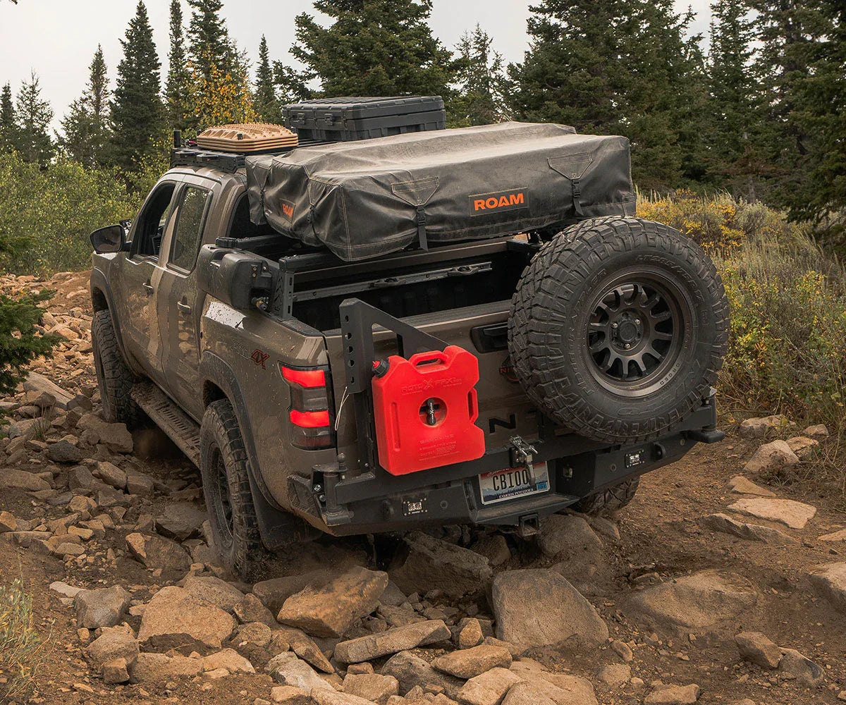 Off-road truck outfitted for overlanding with rooftop tent, spare tire, and gear on rocky trail