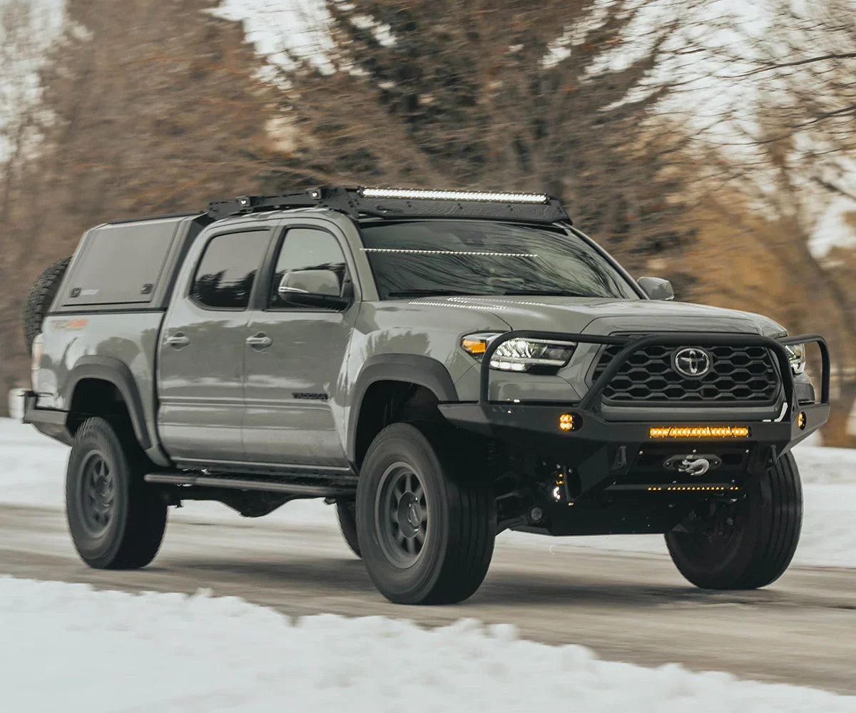 Toyota Tacoma overland build with rock sliders, off-road front bumper, and roof rack in snow