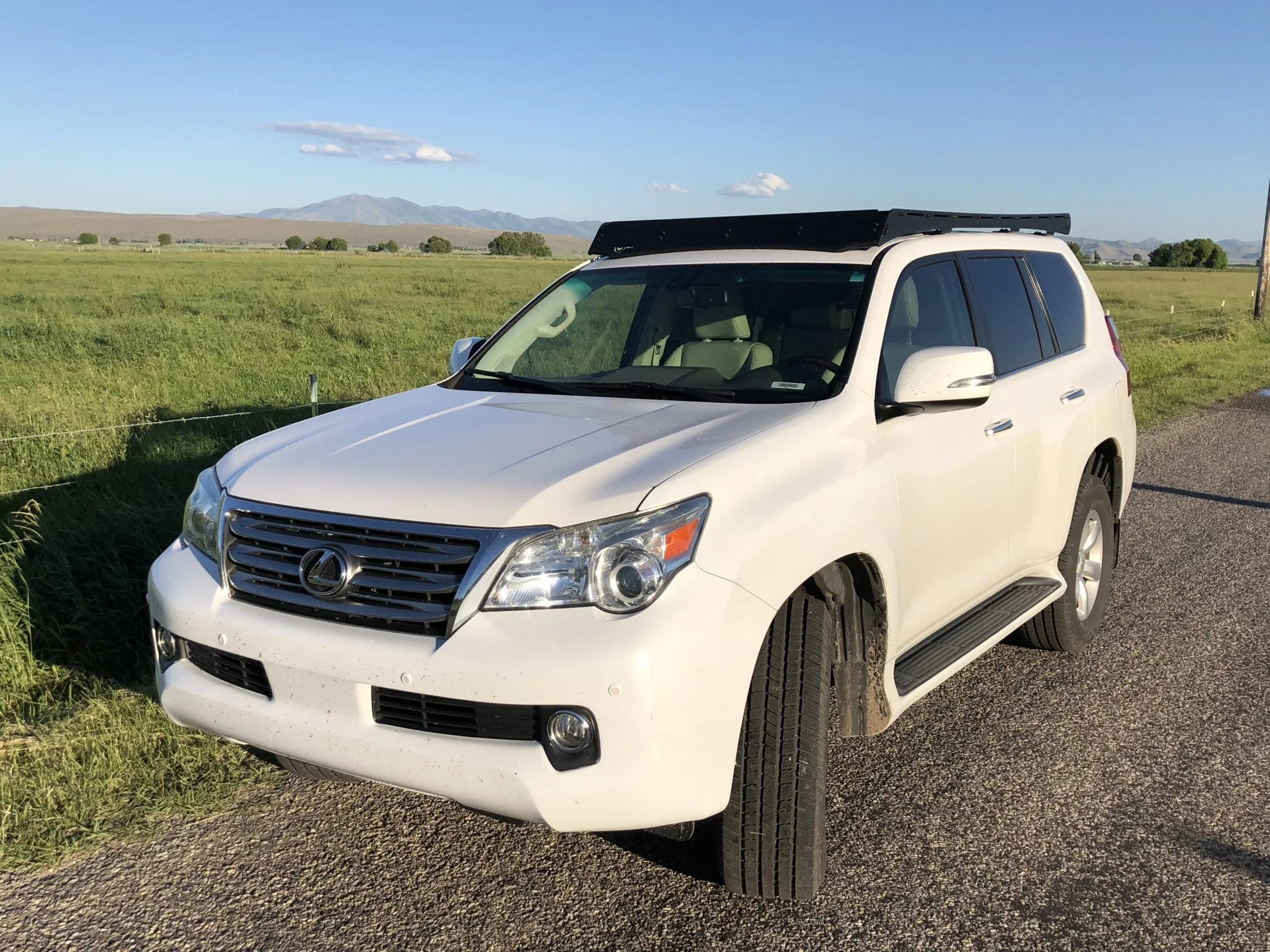 White Lexus GX 460 SUV with roof rack parked on rural road, green field background