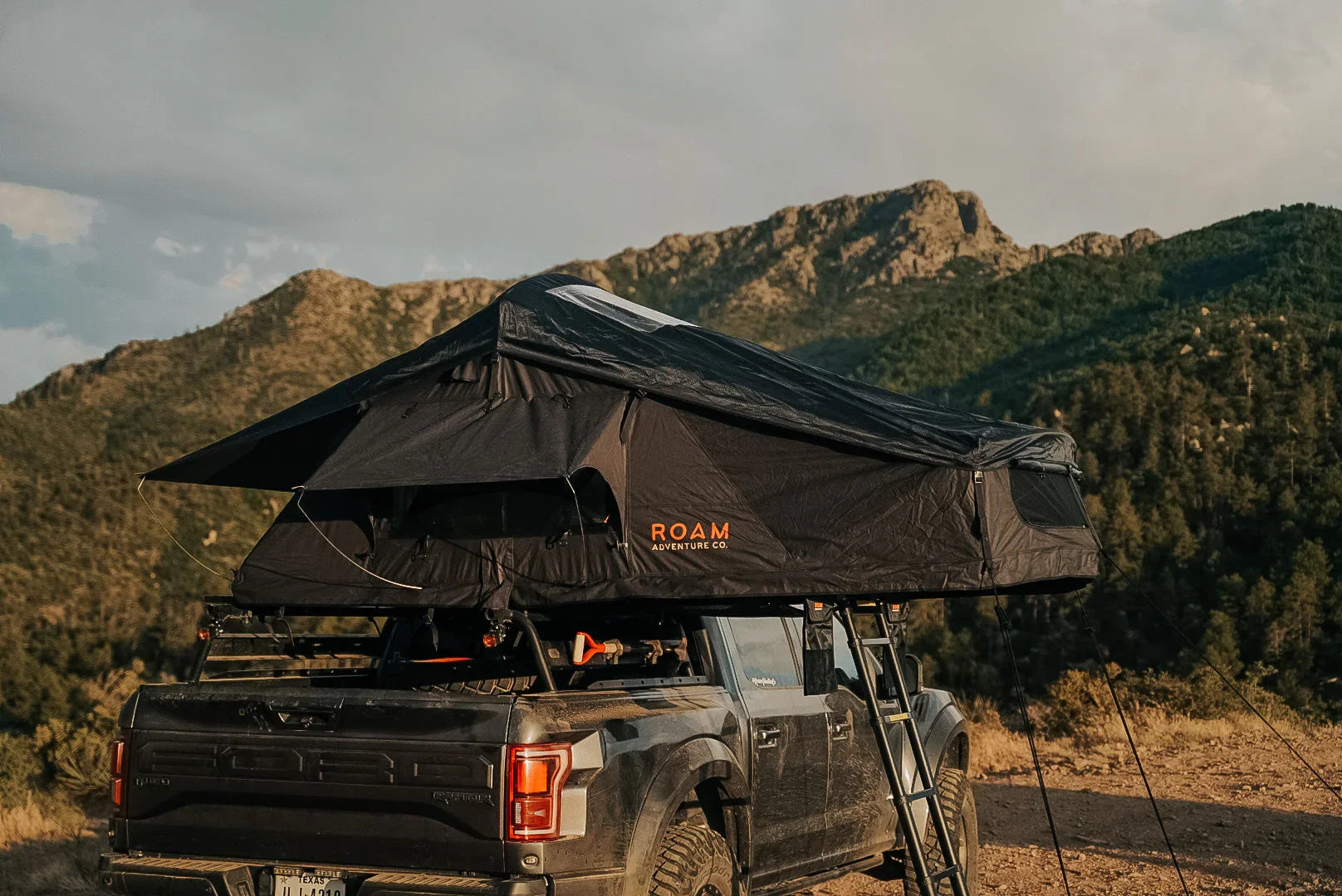 Ford truck with rooftop tent and ladder, parked outdoors with mountains in the background
