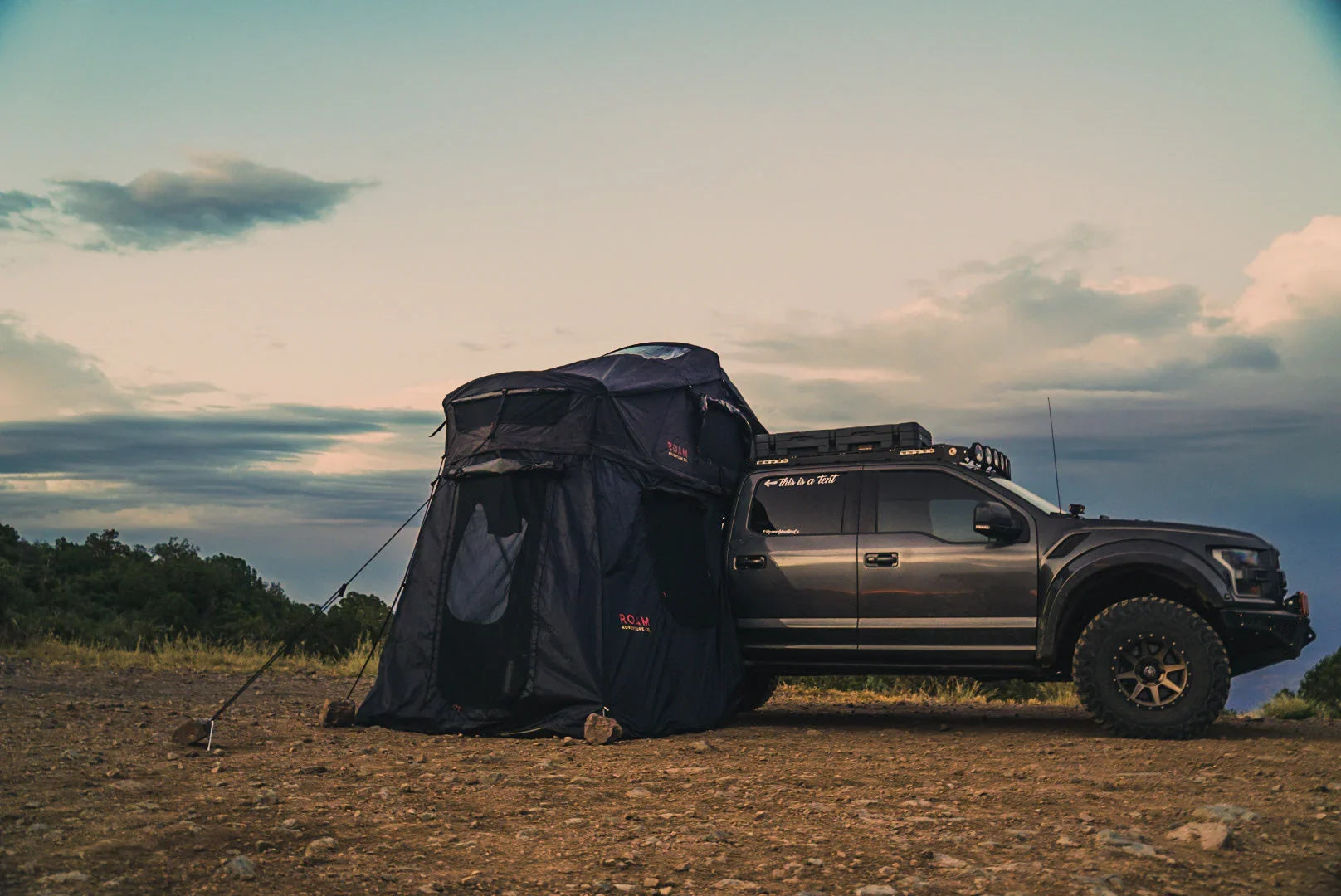 Overland truck with rooftop tent and annex set up at campsite under evening sky