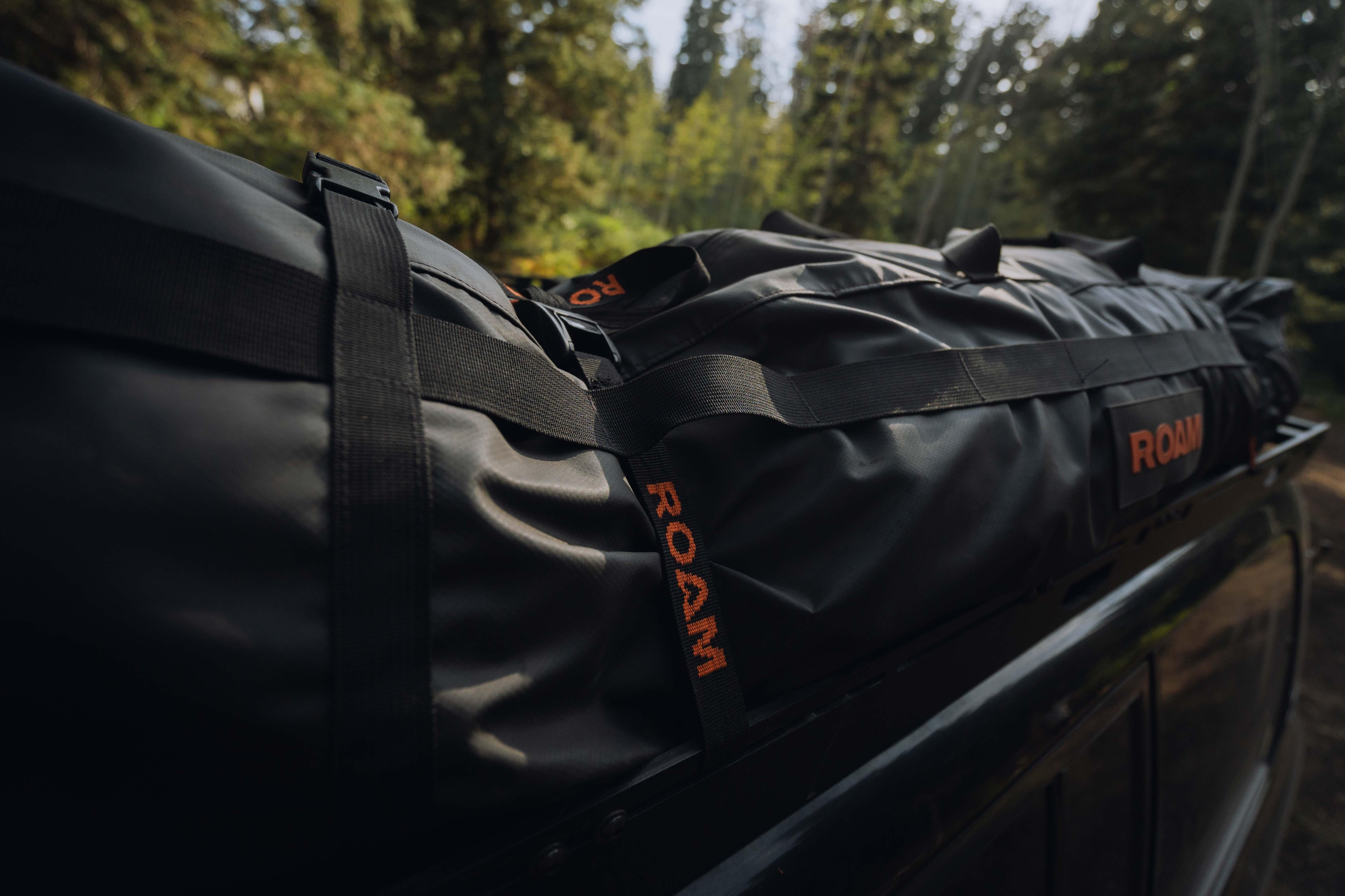 Black ROAM rooftop cargo bag secured on vehicle, forest adventure setting