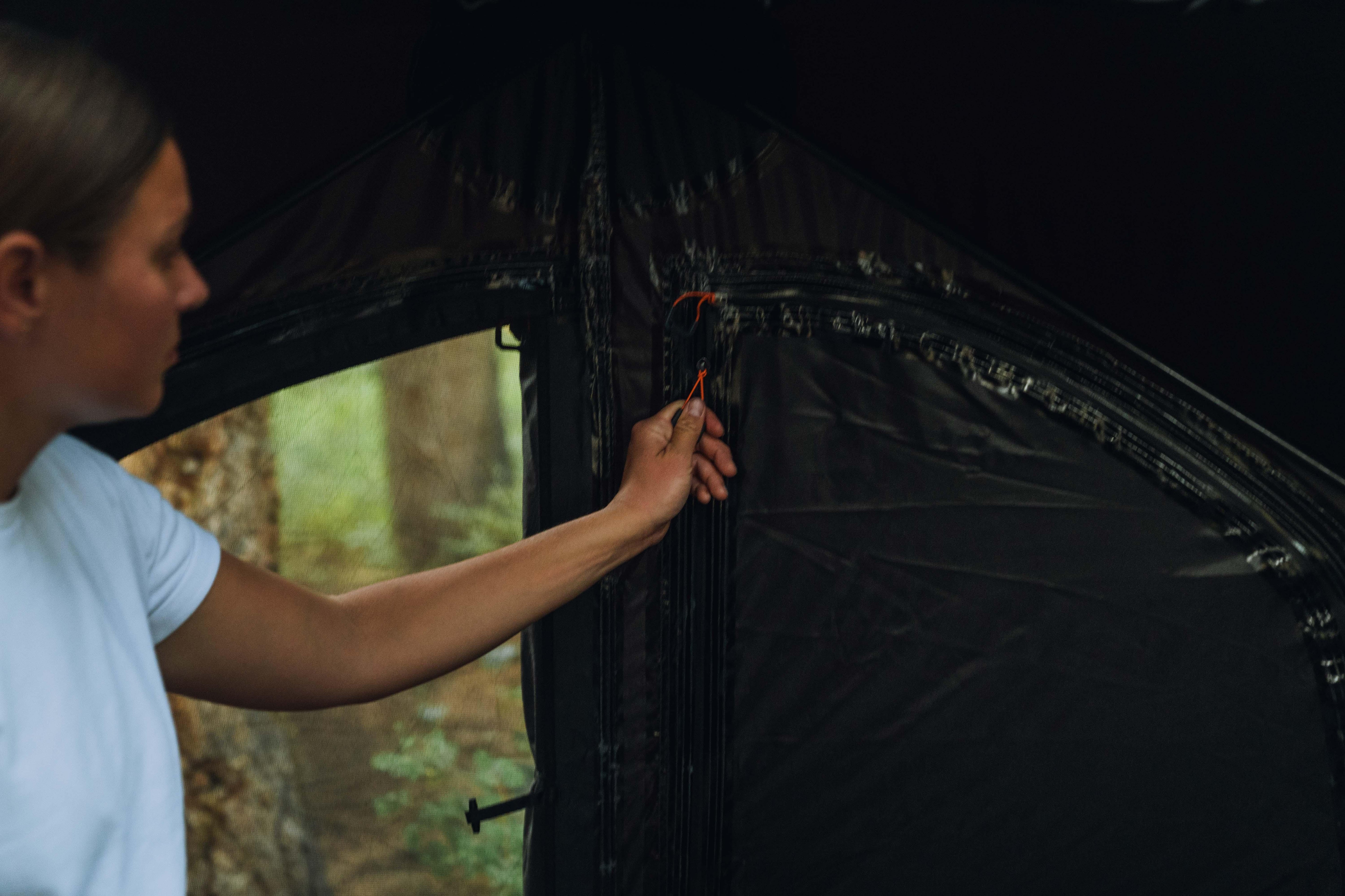 Person zipping a black camping tent in a forest setting, closeup view