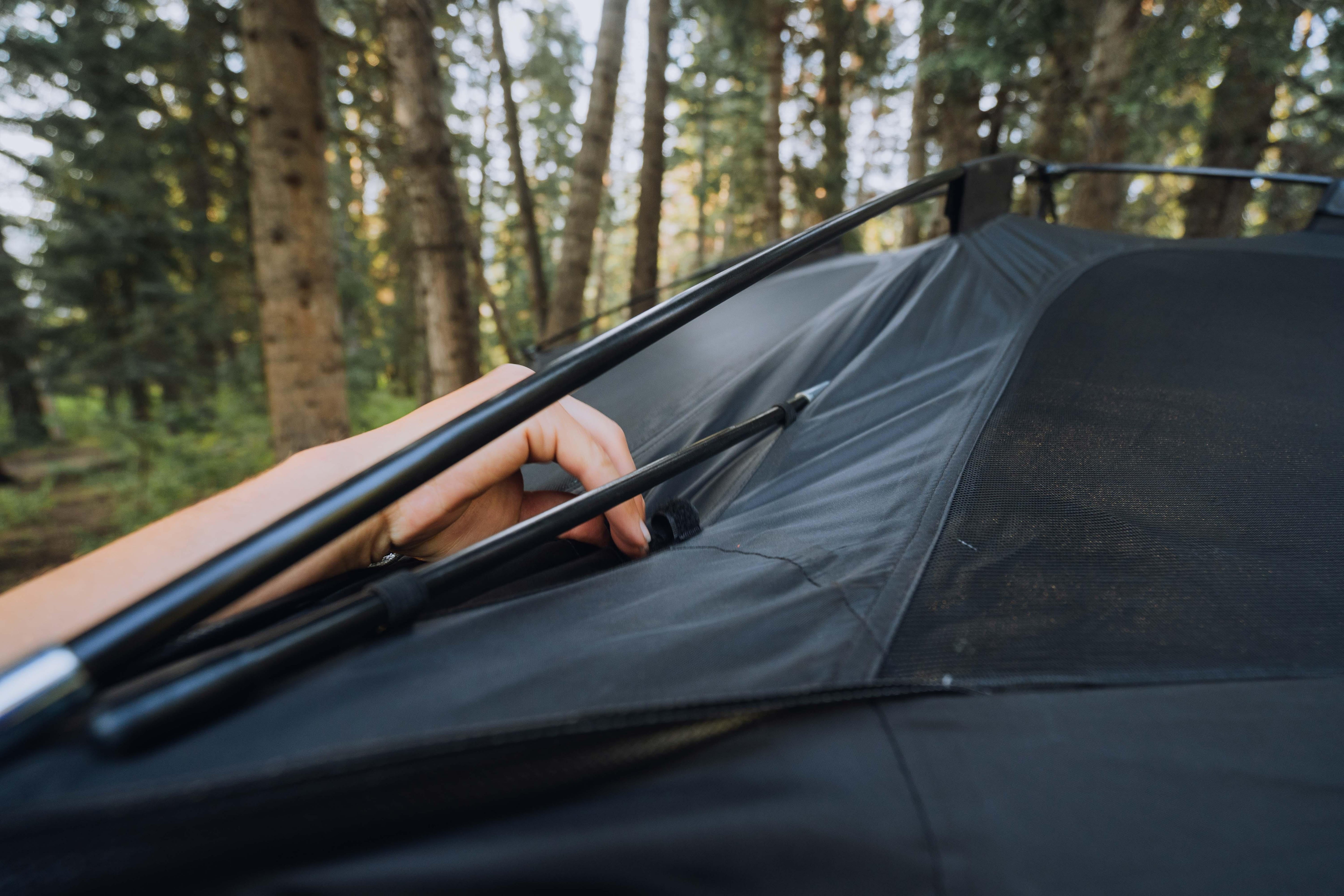 Hand assembling rooftop tent frame in forest campsite